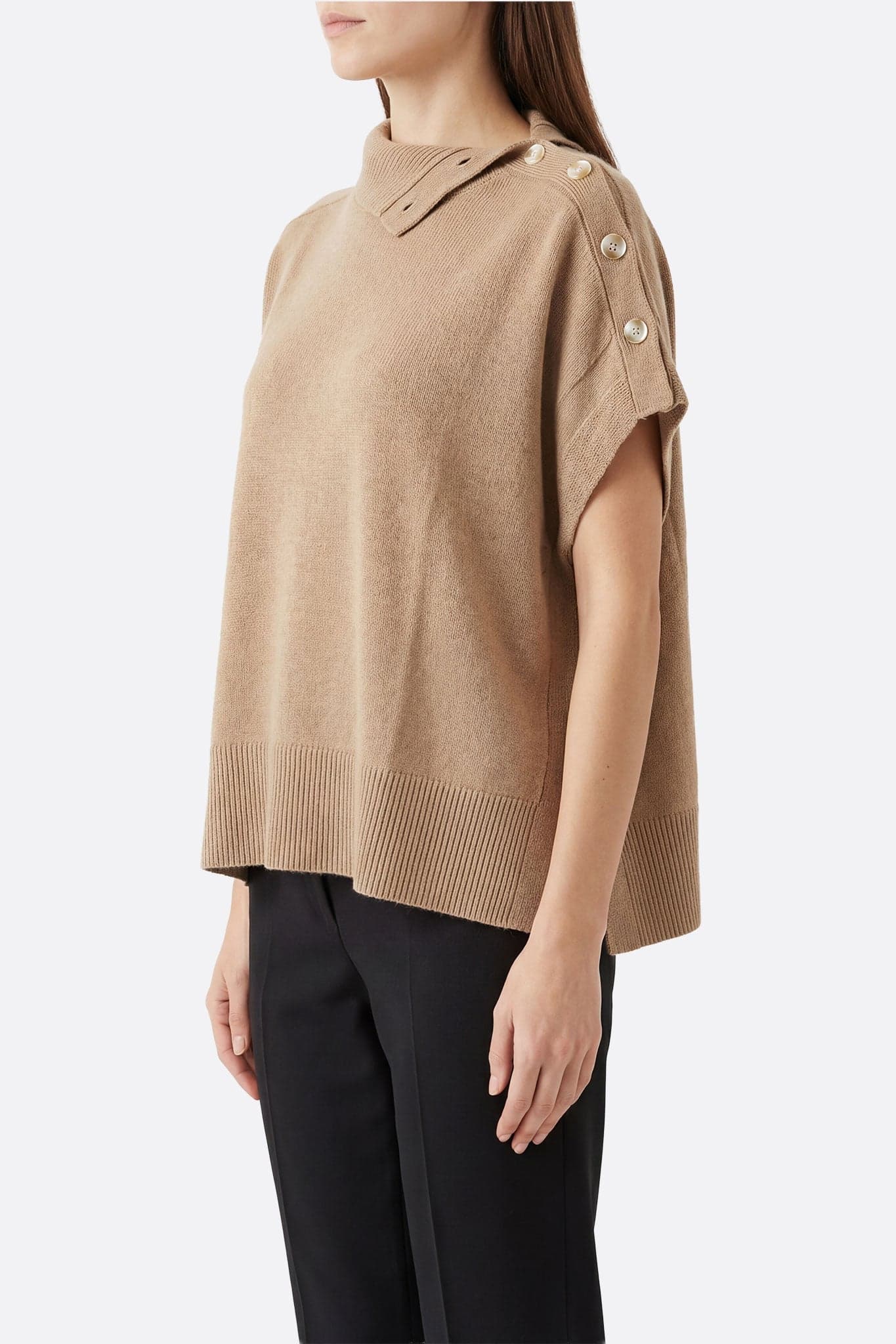 Detail of the buttoned stand-up collar of the beige poncho sweater, ideal for an elegant look on winter evenings.