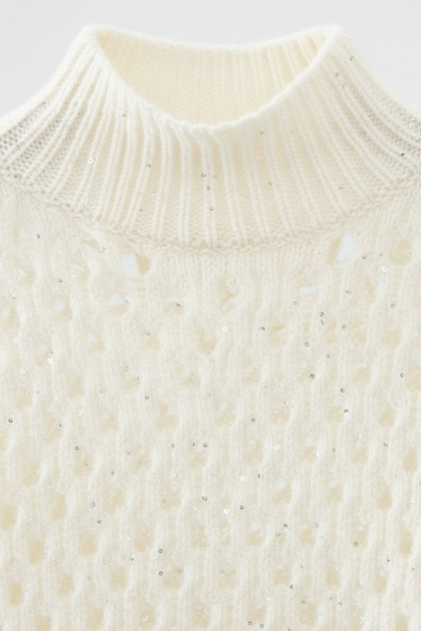 Detail des weißen Lochmuster-Kaschmirpullovers mit Stehkragen, Paillettenverzierungen für einen raffinierten und gemütlichen Look.