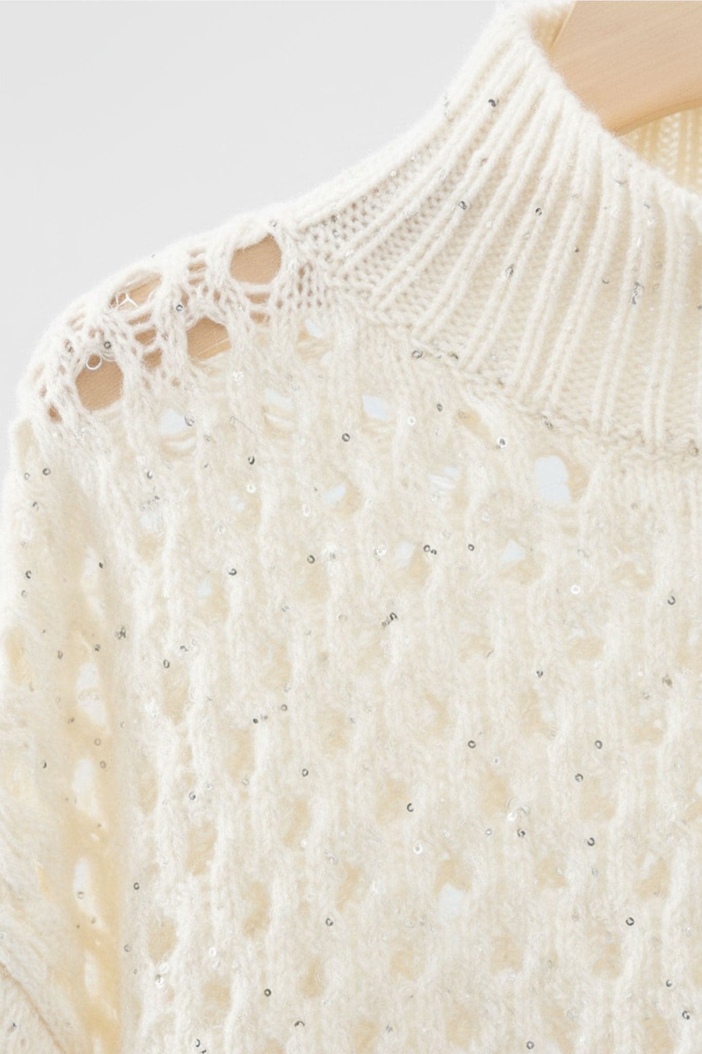 Detail des weißen Kaschmirpullovers mit Lochmuster-Stehkragen und Pailletten, ideal für einen eleganten Look an einem Herbstabend.