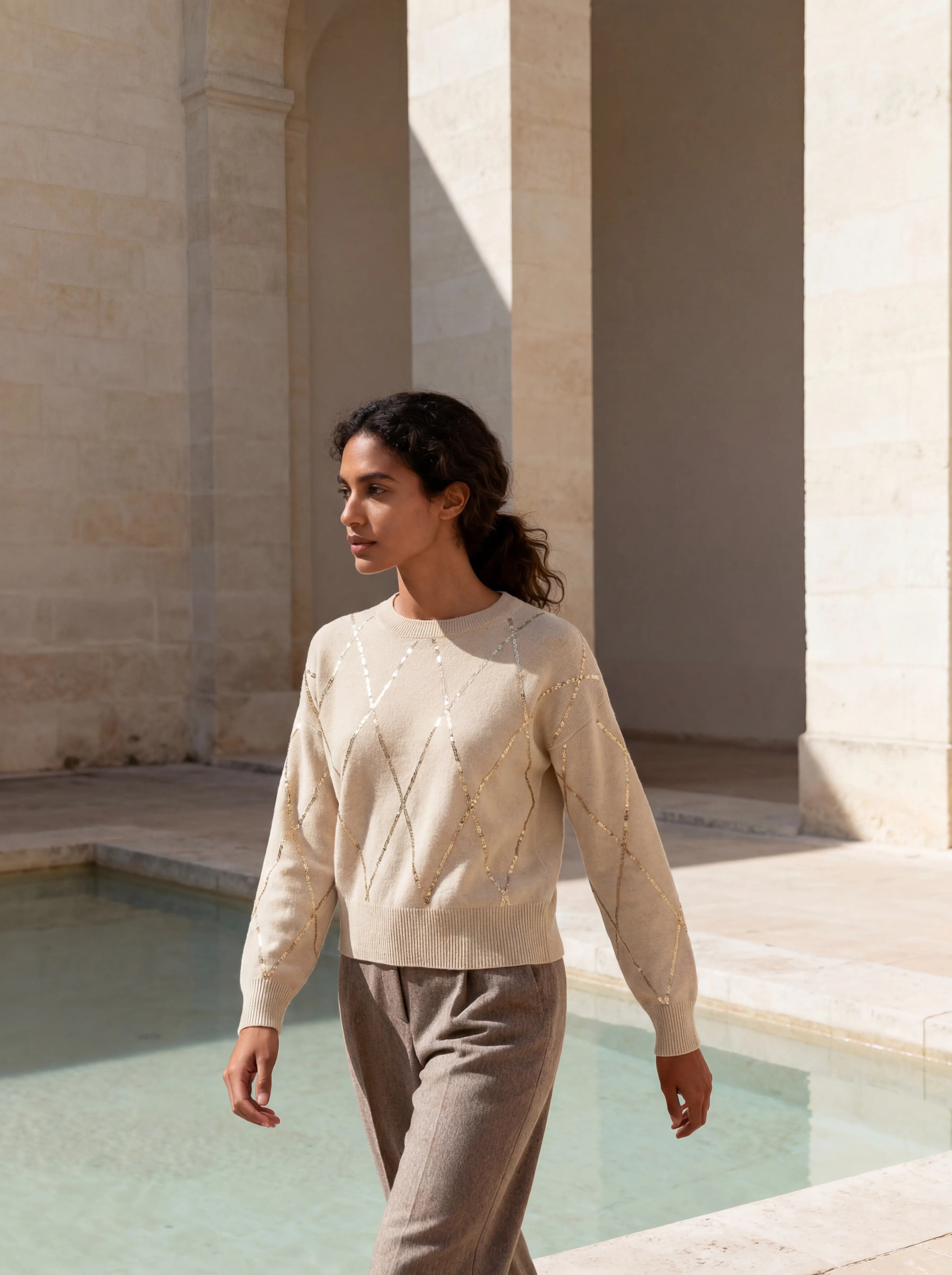 Profile model wearing a beige mélange wool pull with shimmering motifs