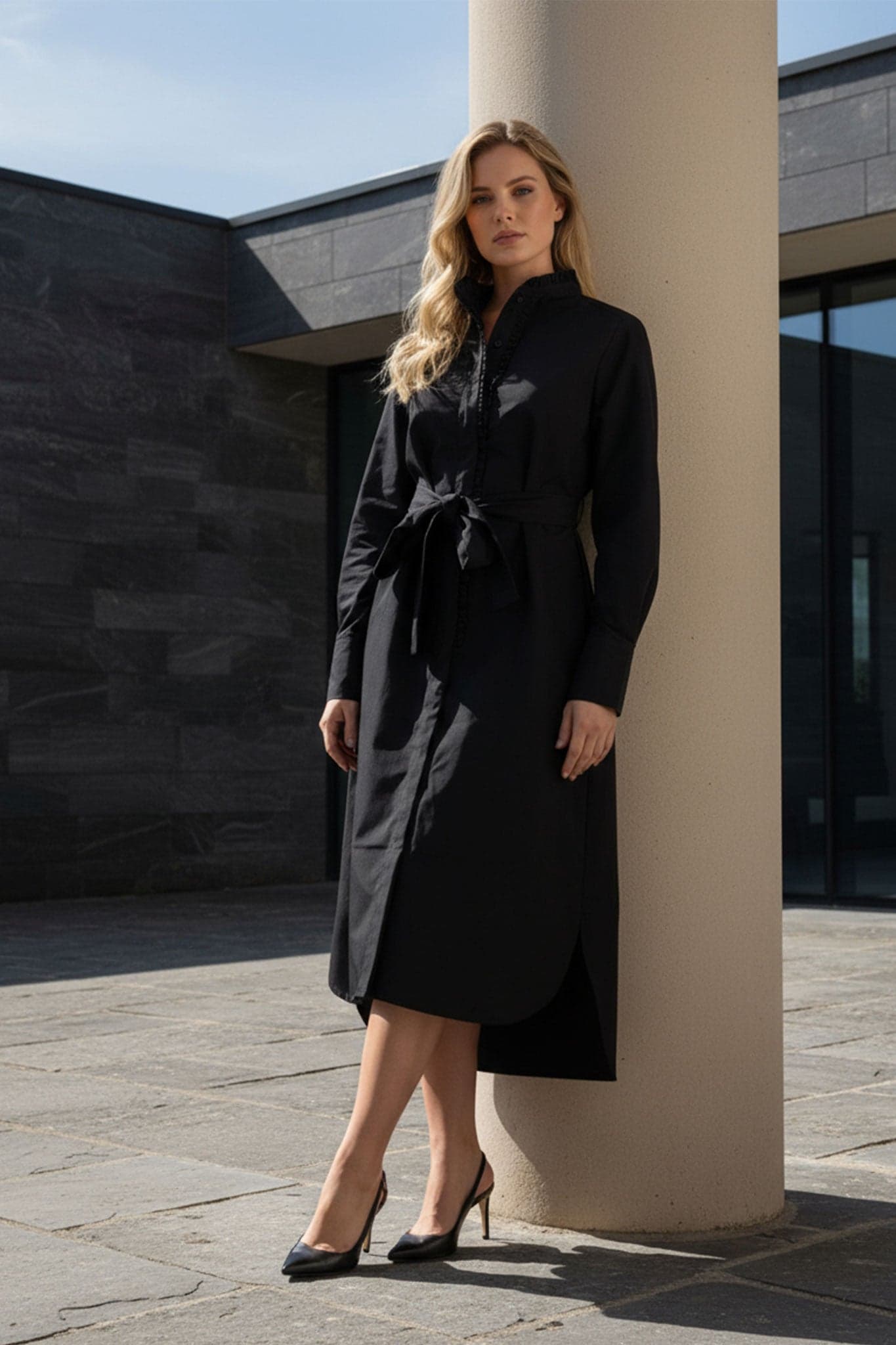 Dettaglio dell'abito camicia lungo nero, che mette in evidenza la cintura e la texture elegante del tessuto.