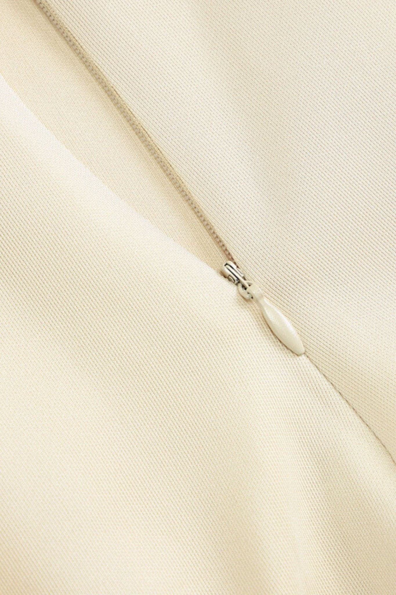 Detalle elegante del vestido corto evasé beige, resaltando su escote audaz y su fluidez refinada.