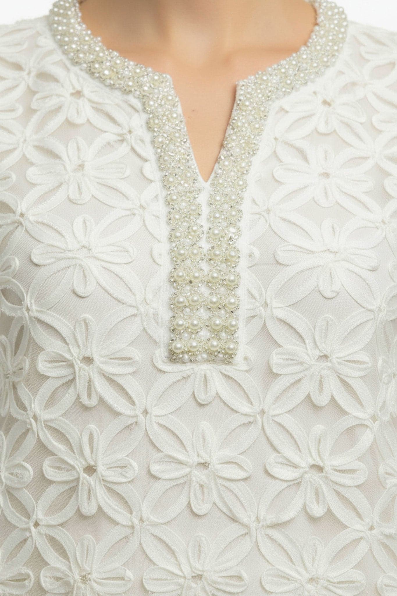 Zoom sur la broderie florale perlée d'une robe courte blanche, ajoutant une touche d'élégance à votre look de jour.