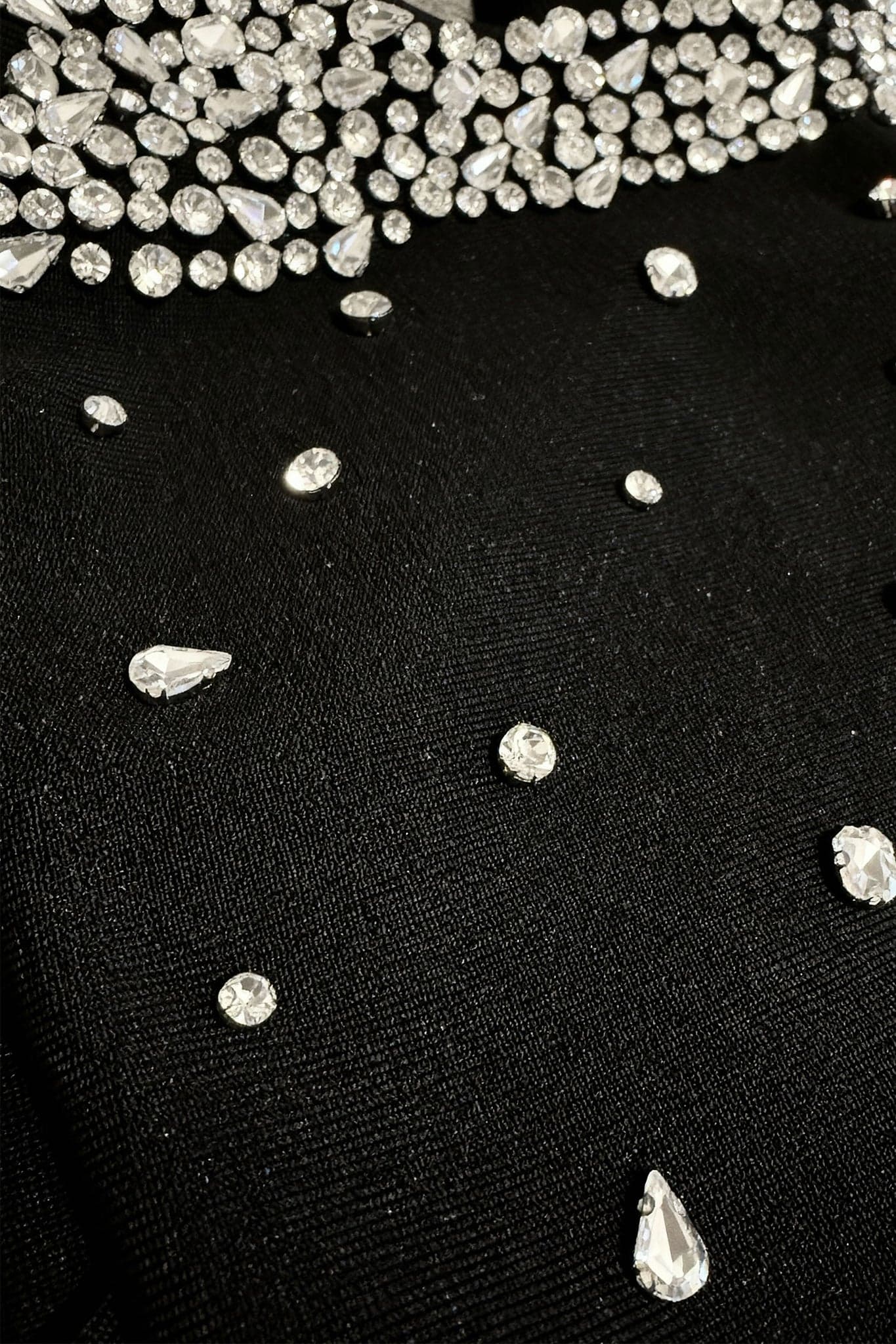 Captivating detail of a short black dress highlighting the shining pearls and refined bows at the shoulders.