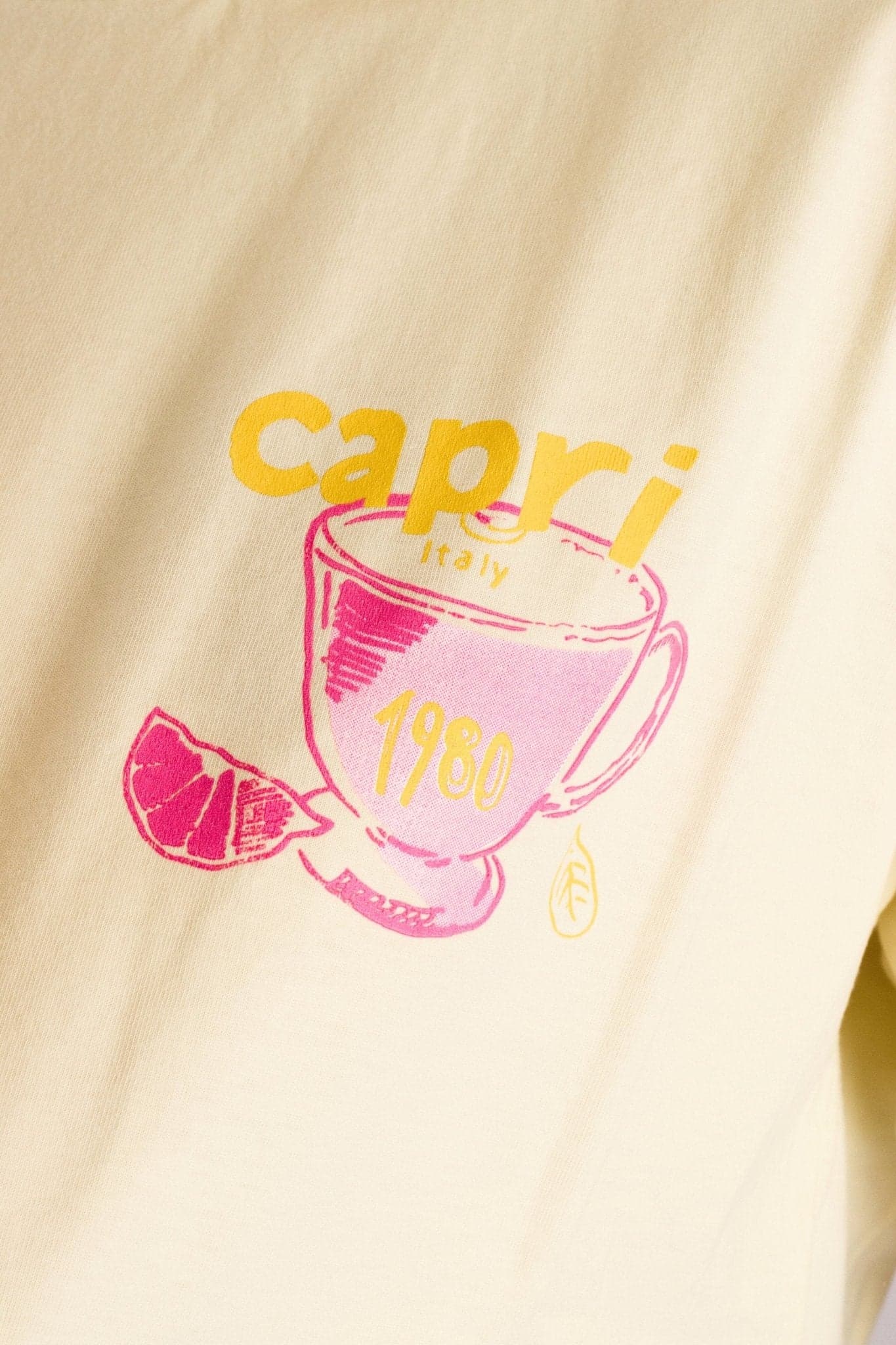 Détail du t-shirt ample jaune pastel, mettant en avant son imprimé Capri, parfait pour une allure chic au quotidien.