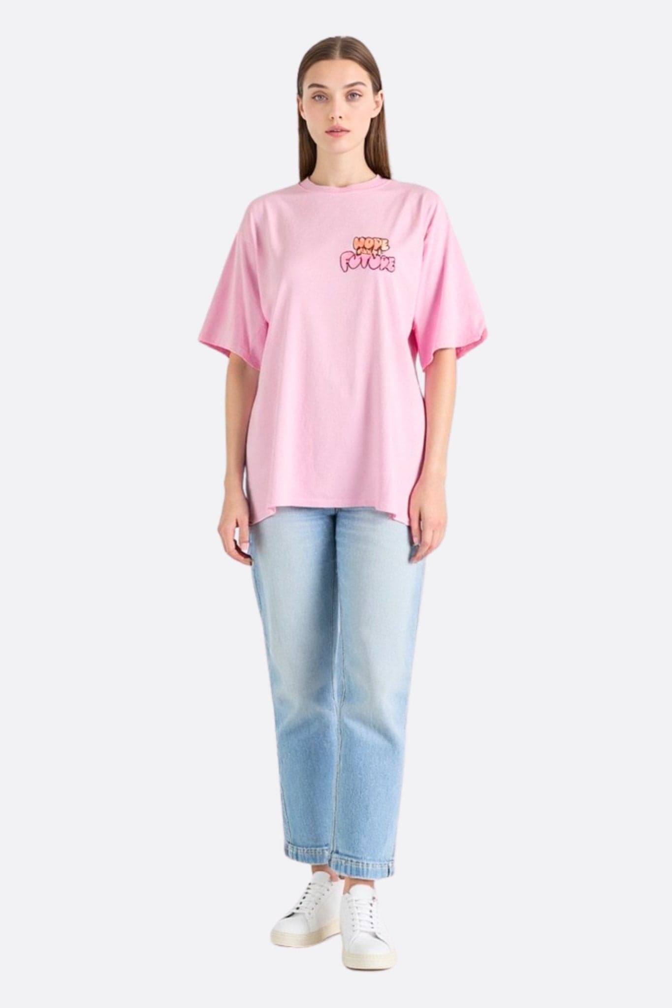 Primo piano della t-shirt oversize in cotone rosa pastello, che evidenzia il suo messaggio di speranza, ideale per un look chic e...