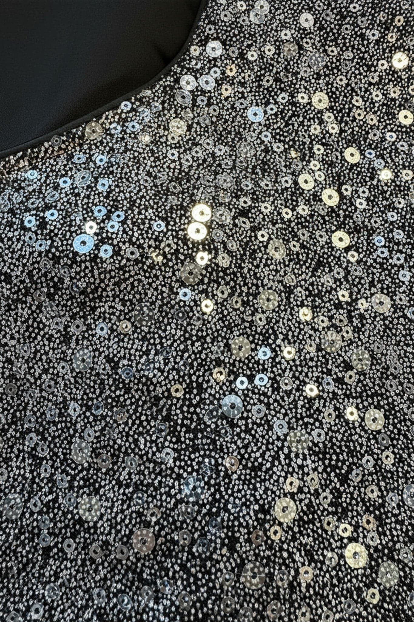 Top noir à sequins argent capturant la lumière, mise en valeur des poignets plissés, parfait pour une soirée élégante.