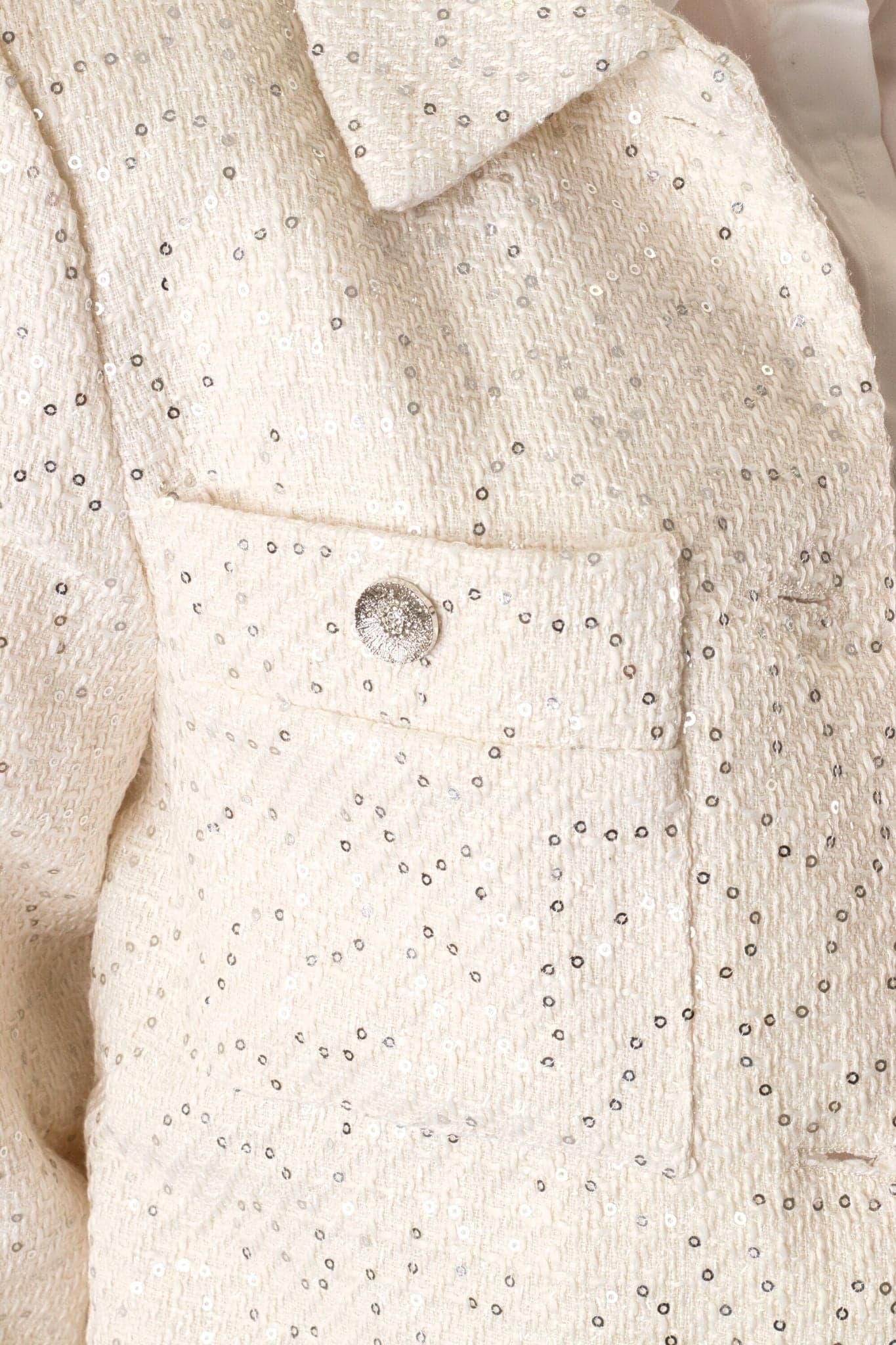 Veste courte en tweed écru à sequins, un modèle éclatant pour ajouter une touche distinguée à vos soirées habillées.