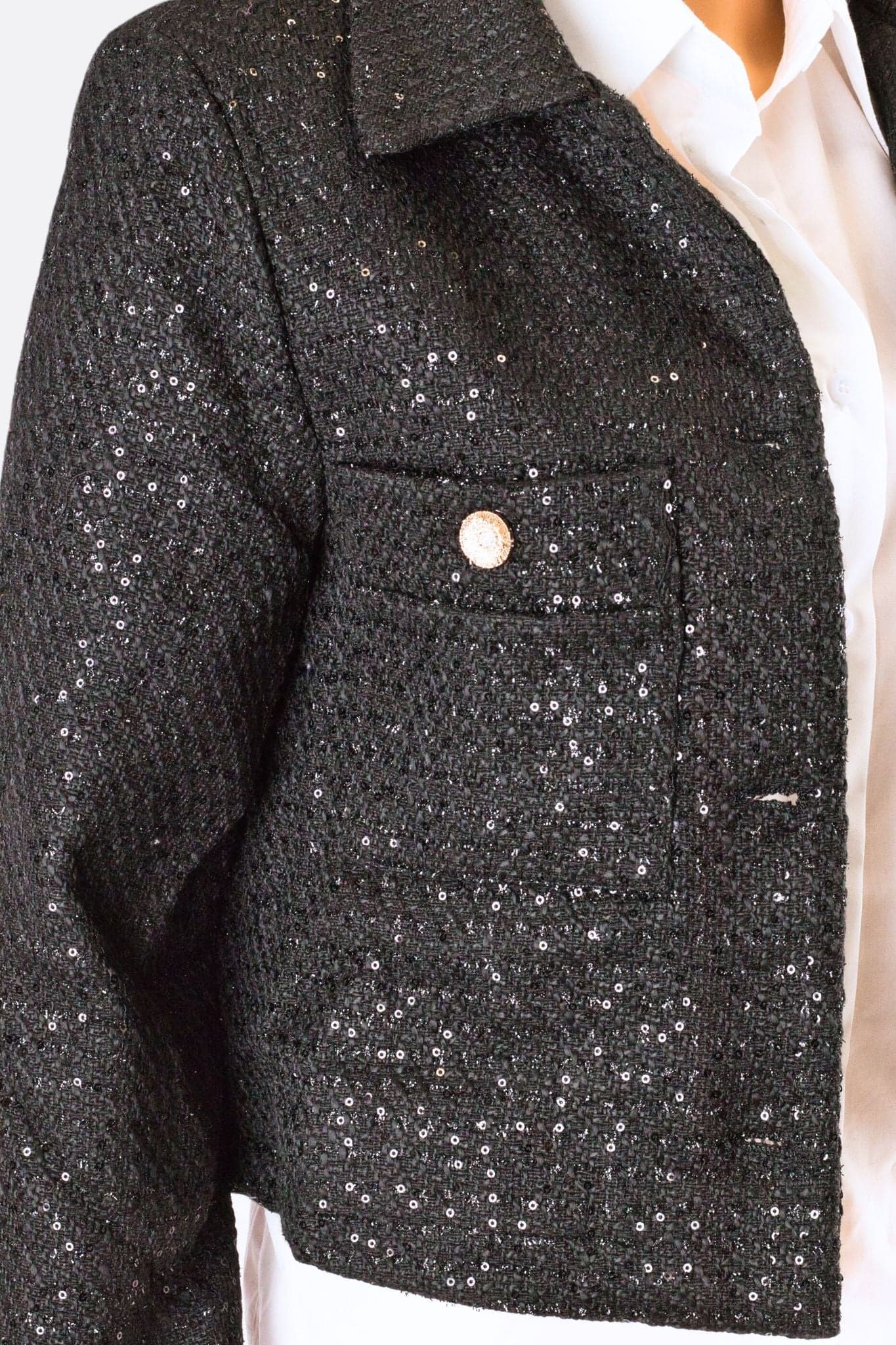 Detalles brillantes del chaquetín corto de tweed negro adornado con lentejuelas, perfecto para realzar un look de noche refinado.