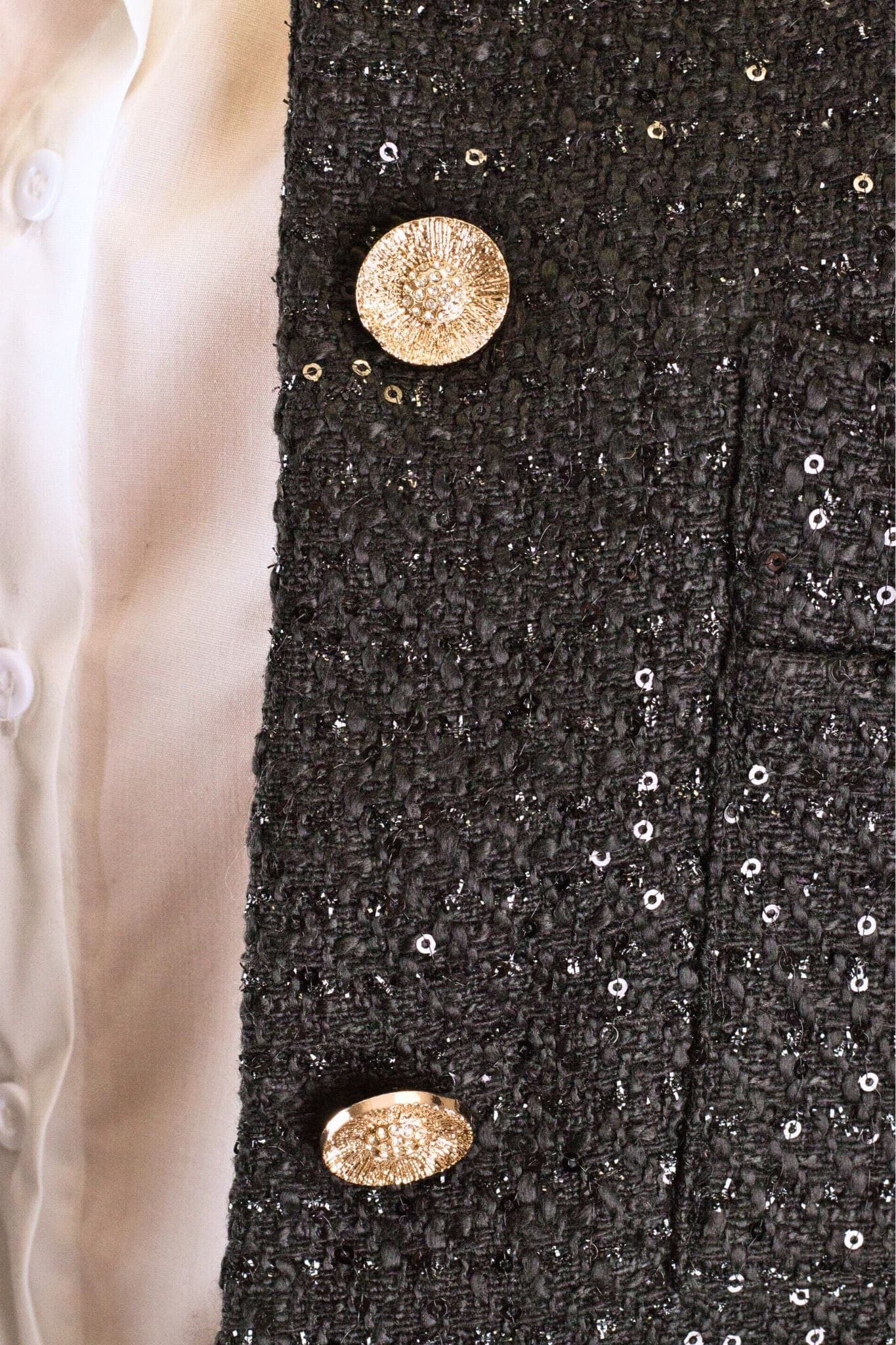 Vista cercana del chaquetín corto de tweed negro con lentejuelas, perfecto para añadir un toque glamuroso a un look de noche.