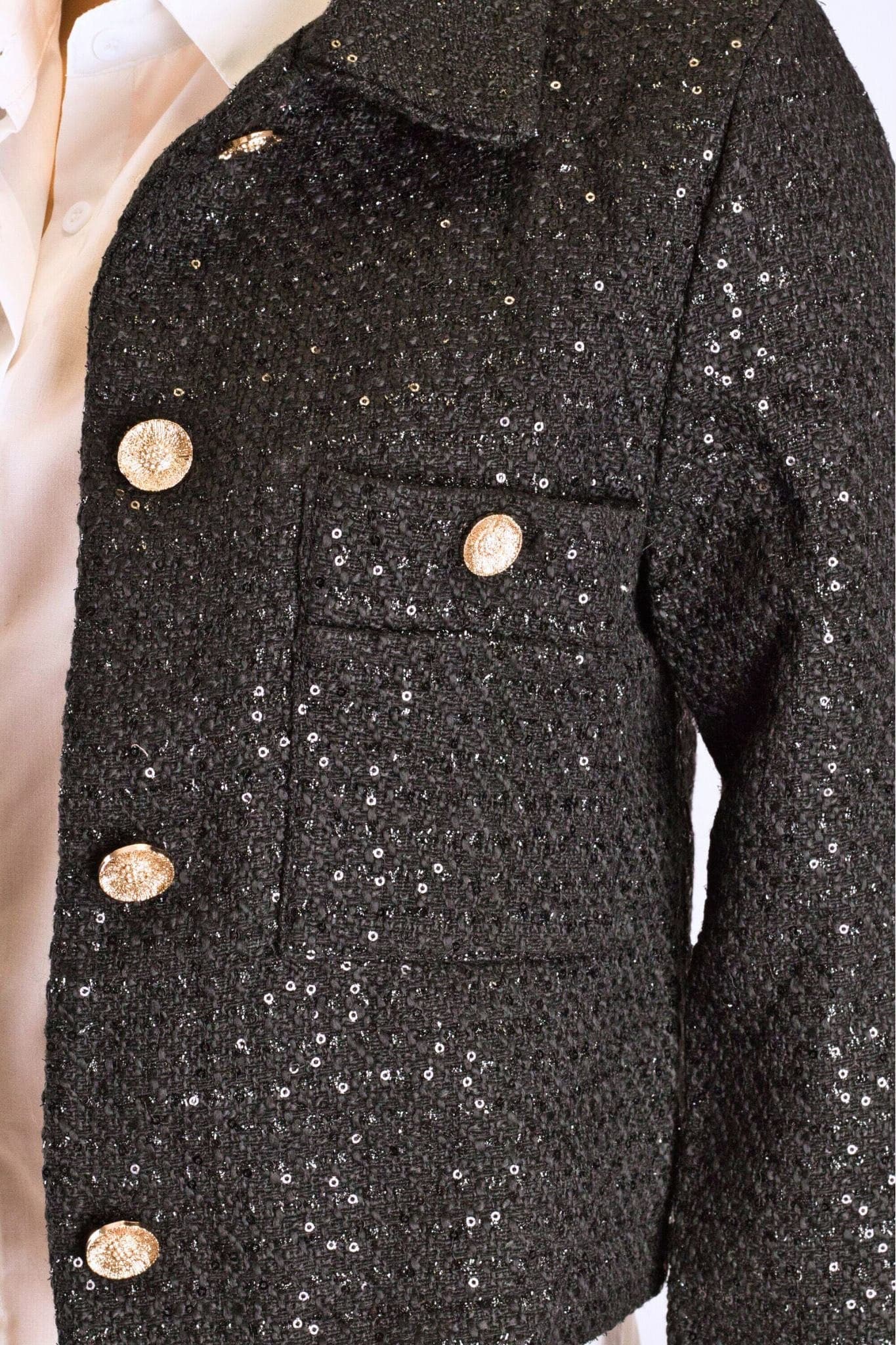 Detalle refinado del chaquetín corto de tweed negro con lentejuelas, perfecto para un look chic en una noche elegante.