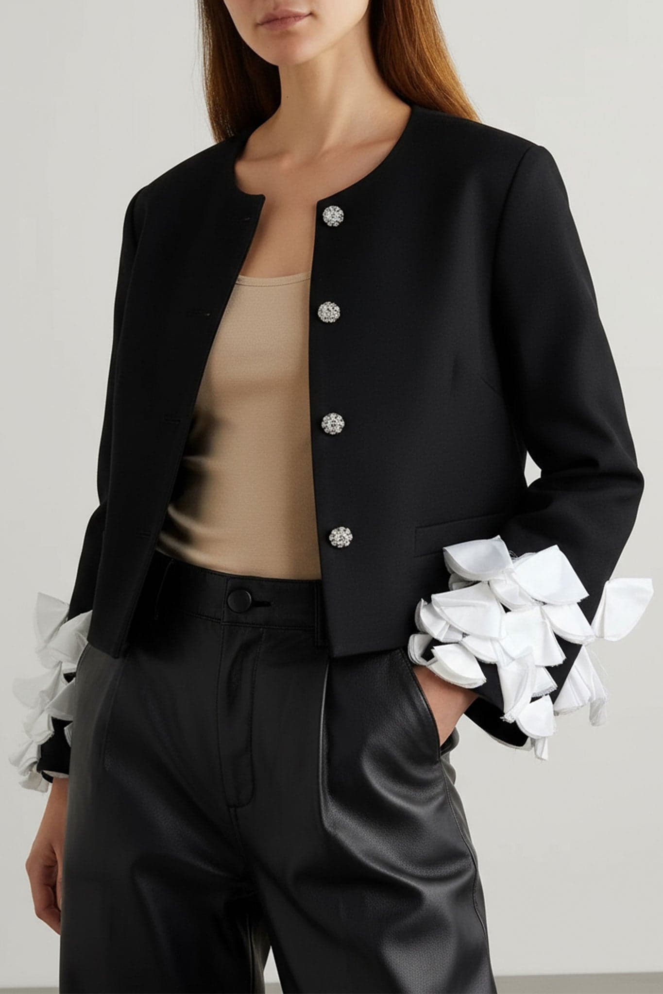 Detaillierte Perspektive der schwarzen Jacke mit Blütenblattärmeln, hervorgehoben durch weiße Federn, perfekt für einen schicken Look.
