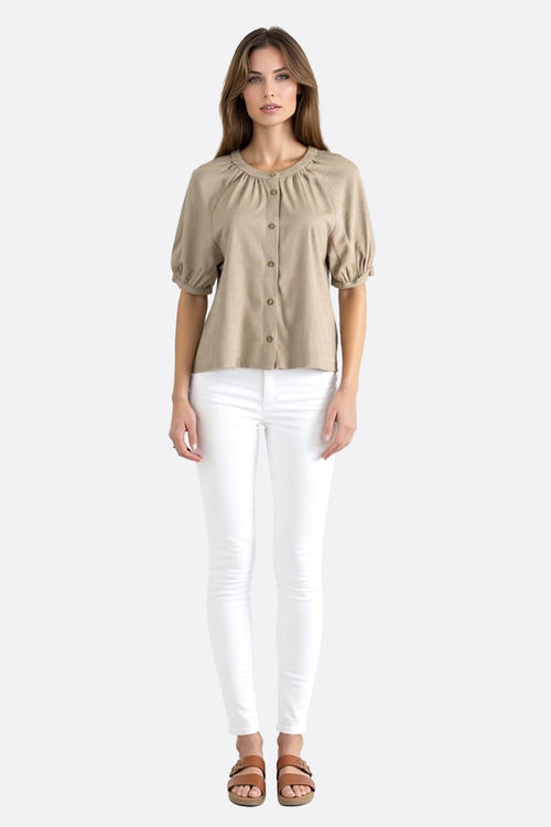 
Zoom sur la blouse beige en lin, soulignant la texture aérienne et les boutons raffinés des manches courtes pour un look...



