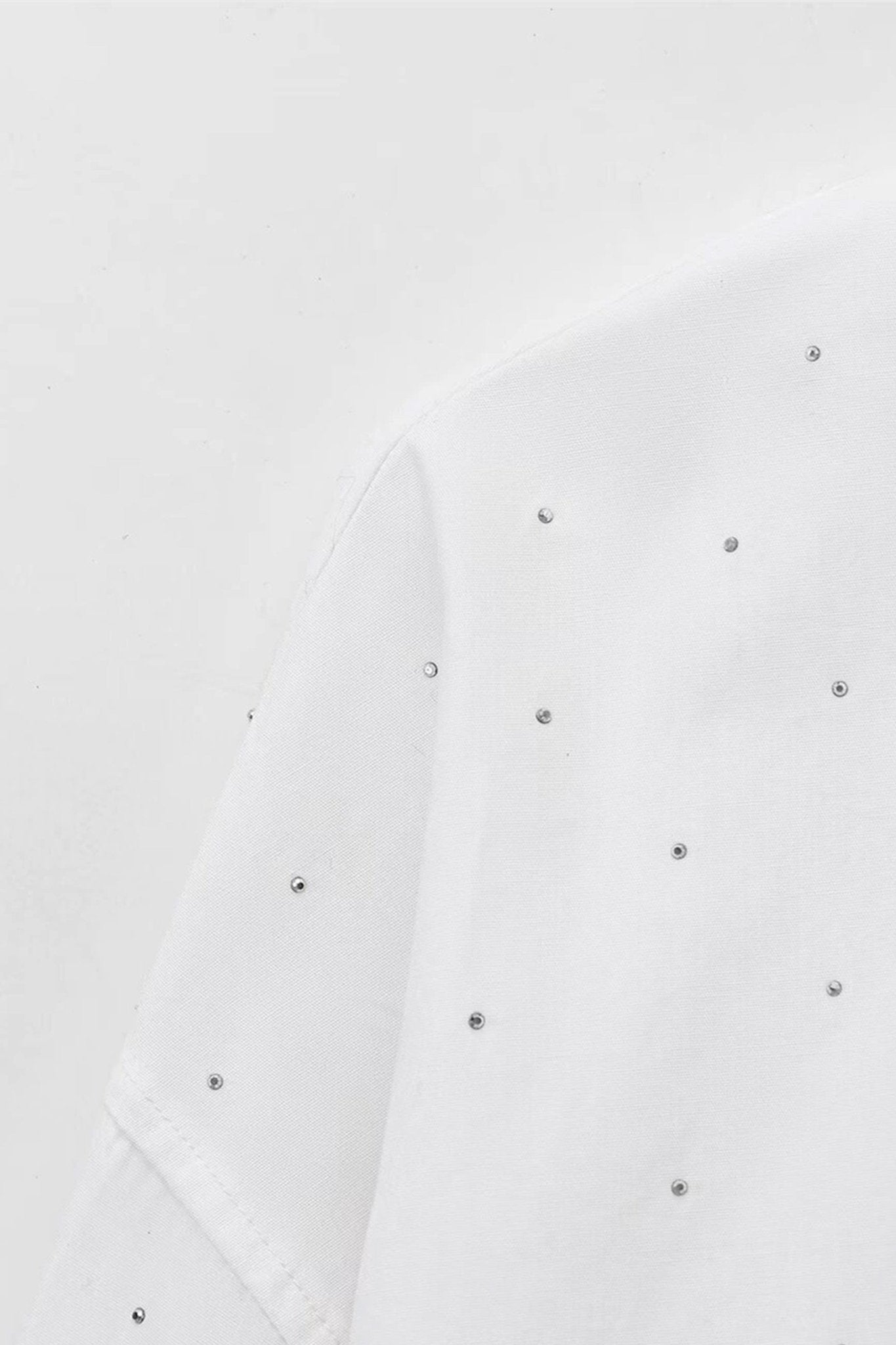 
Vue rapprochée de la chemise blanche oversize ornée de strass, une pièce élégante pour des tenues raffinées en soirée.



