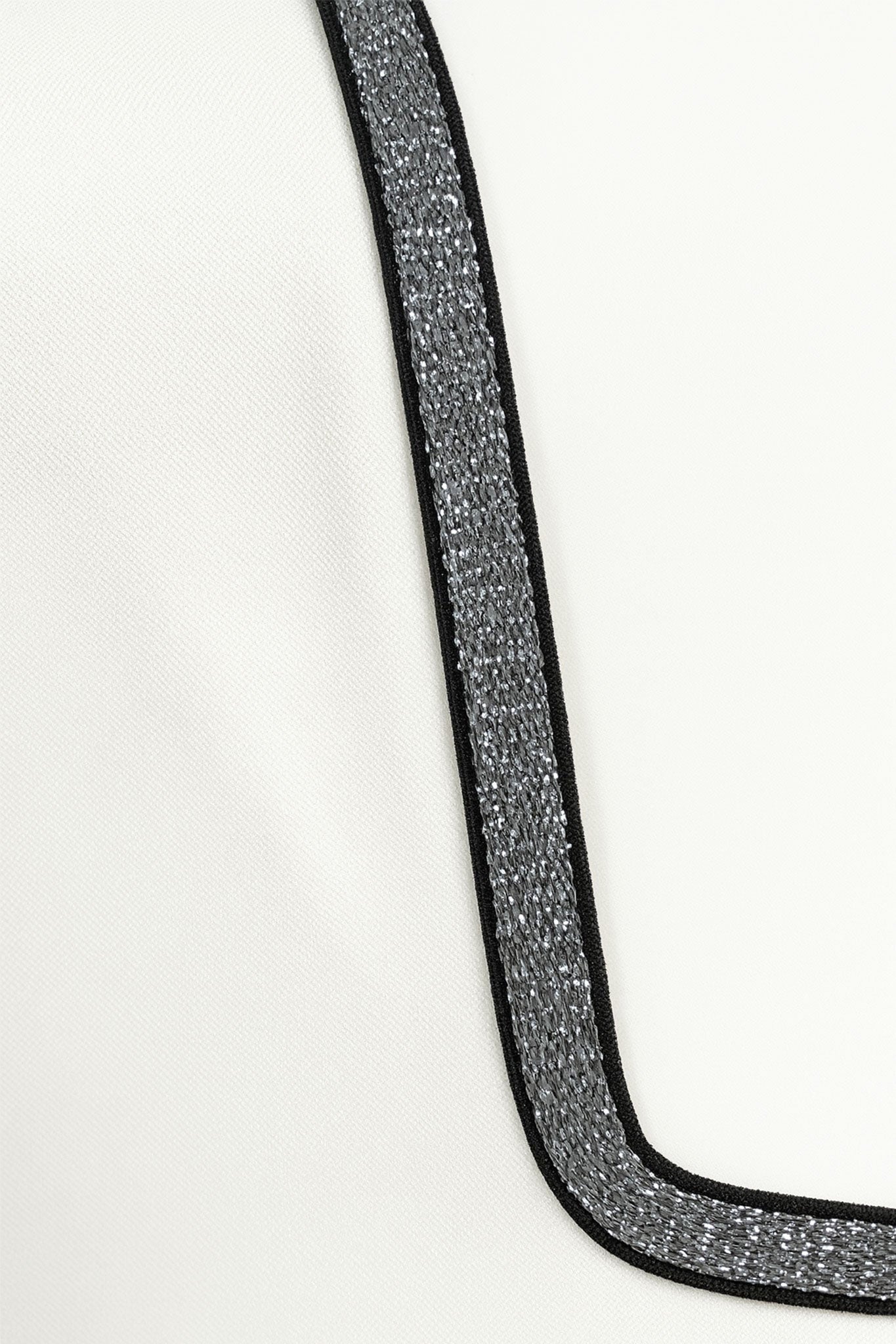 
Détail latéral de la combinaison blanche asymétrique, soulignant la finesse de sa coupe chic et son accent coloré...



