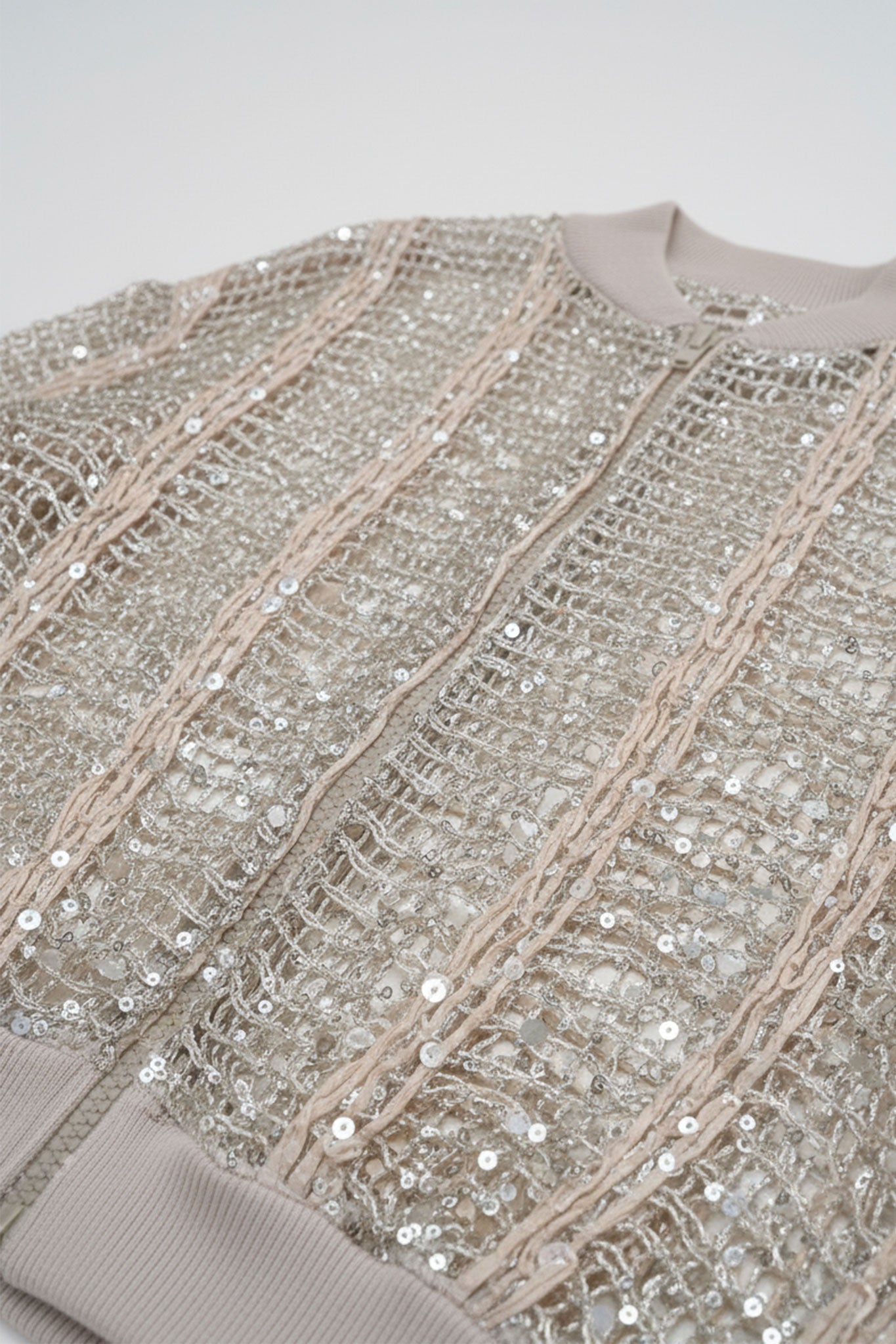 
Détail du gilet bomber ajouré en lin et soie champagne, révélant des sequins scintillants pour une allure raffinée et...



