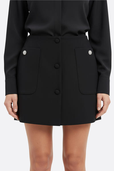 
Zoom sur la jupe noire avec poches généreuses, mettant en lumière les boutons bijoux et sa coupe raffinée.



