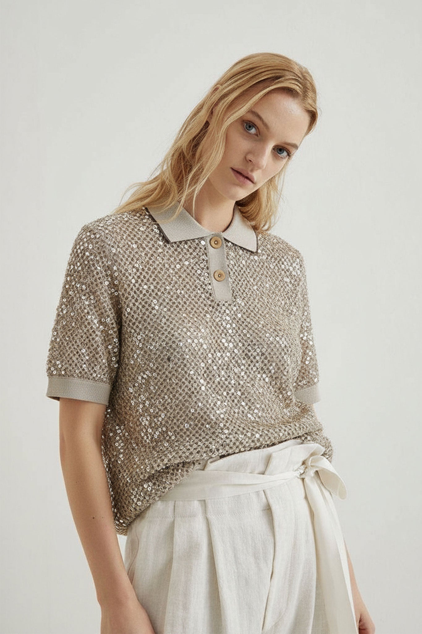Detalle de un polo de manga corta beige sablé en malla calada, embellecido con elegantes sequins tonales, perfecto para...