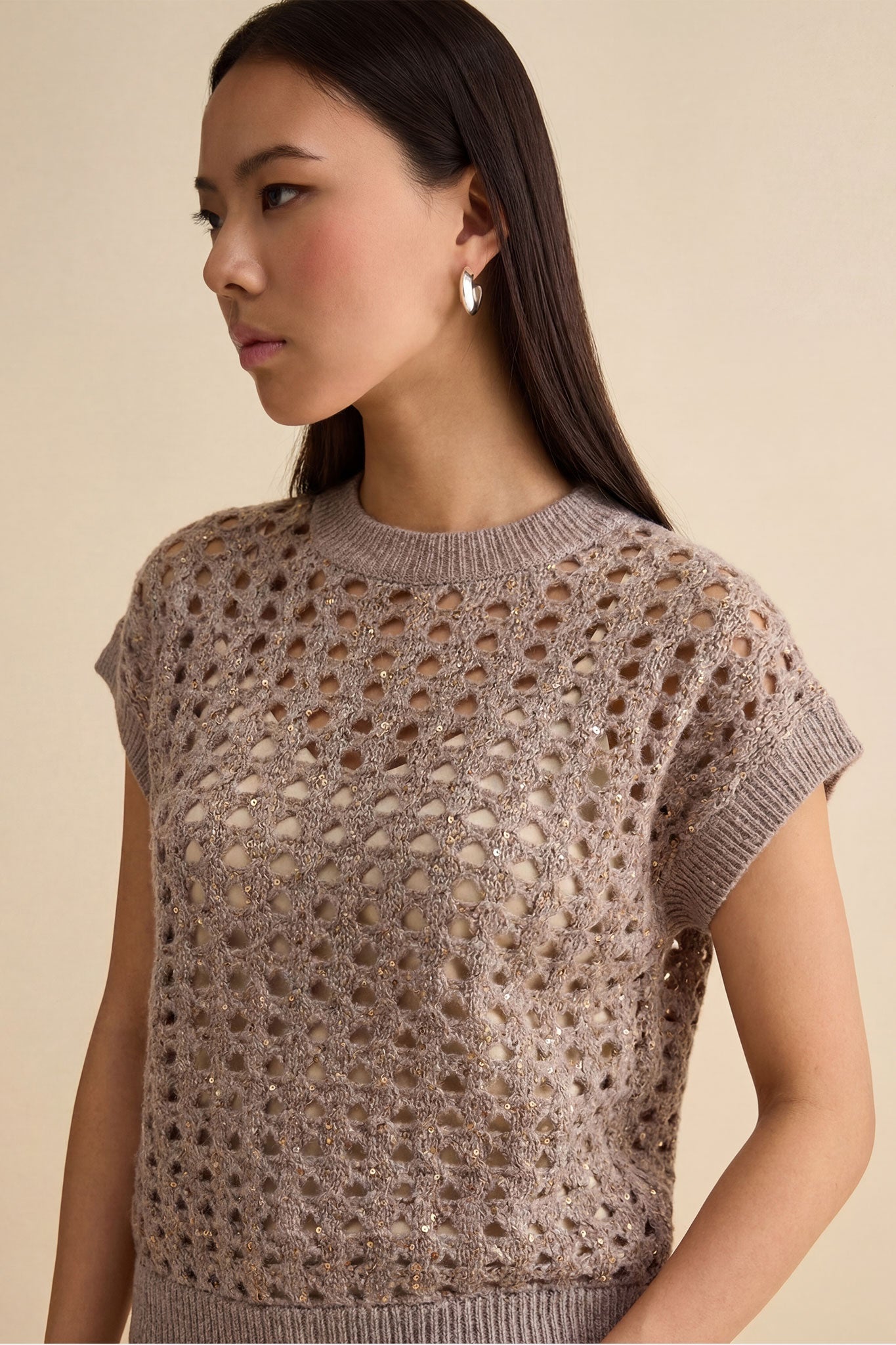 
Détail latéral du pull sans manches en gris taupe, mettant en avant des sequins brillants pour une touche chic et raffinée.



