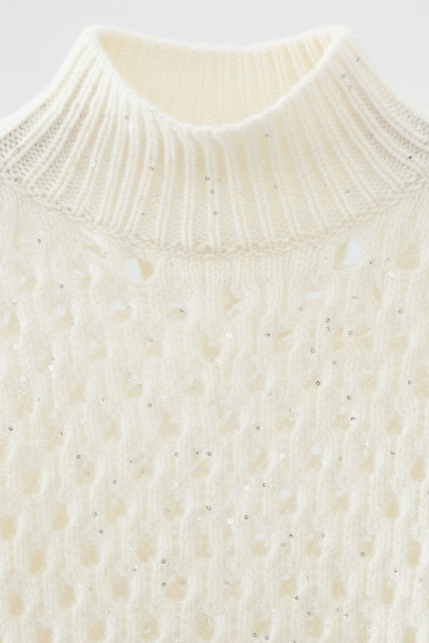 
Détail du pull blanc en cachemire ajouré avec col montant, embellissements en sequins pour un look raffiné et cosy.



