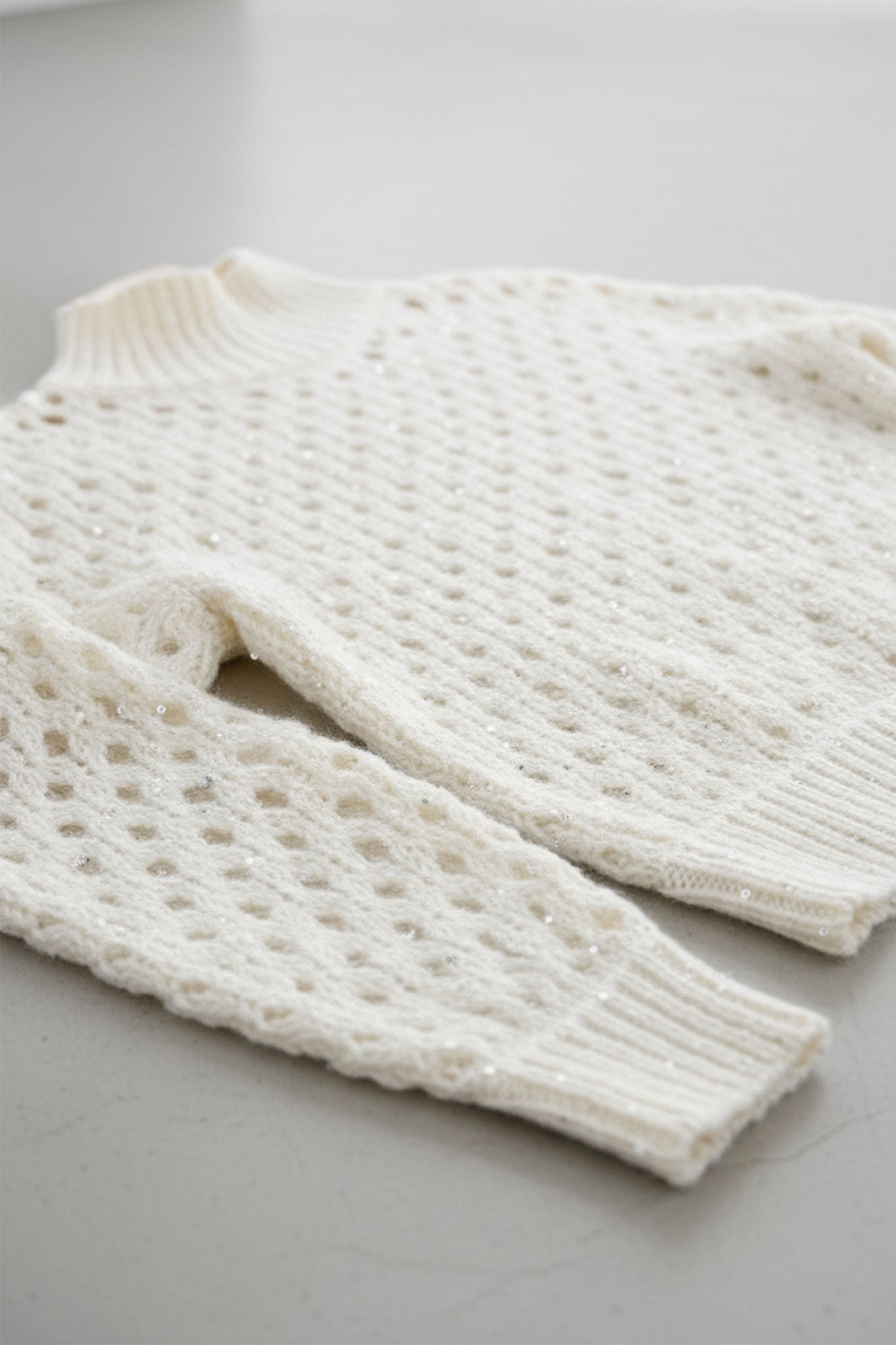 
Vue rapprochée du pull blanc en cachemire ajouré à col montant, mettant en valeur les sequins pour une touche d'élégance...



