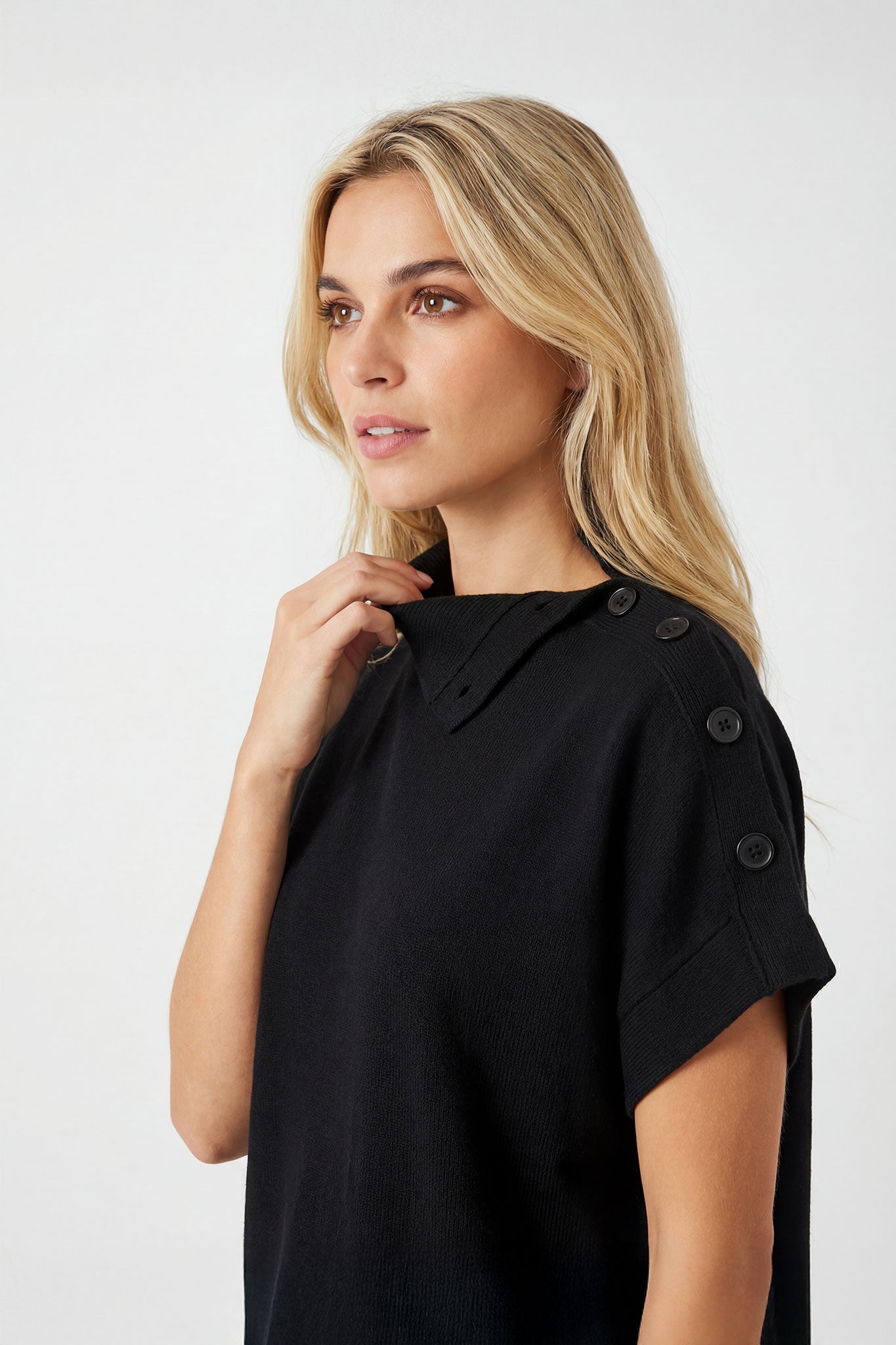 Vue latérale du pull noir oversize à col montant boutonné, soulignant la coupe ample et le chic intemporel pour les...