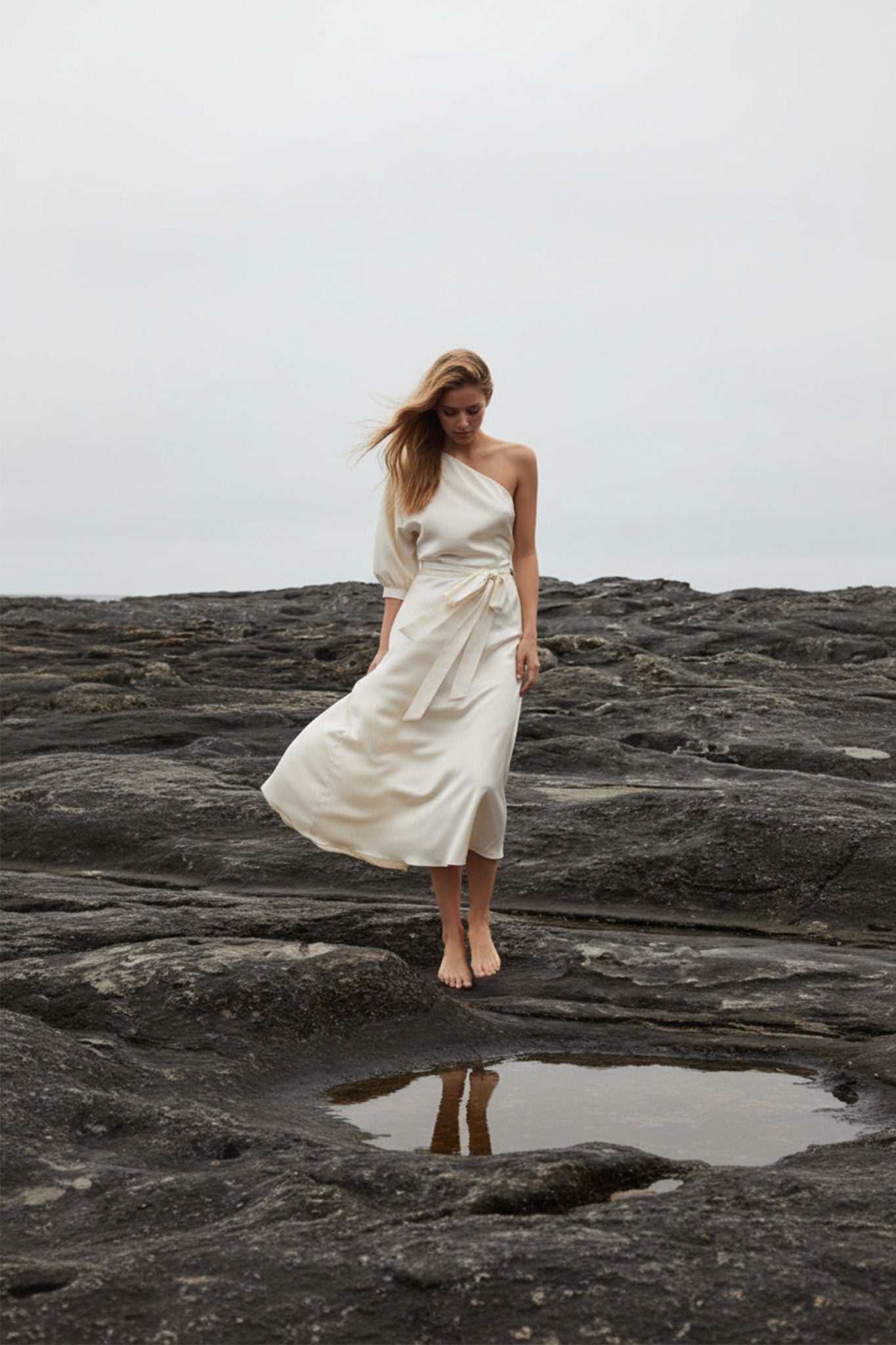 Hinteransicht einer stilvollen asymmetrischen Robe aus luxuriösem Satin in zartem Weiß-Ecru, ideal für elegante...