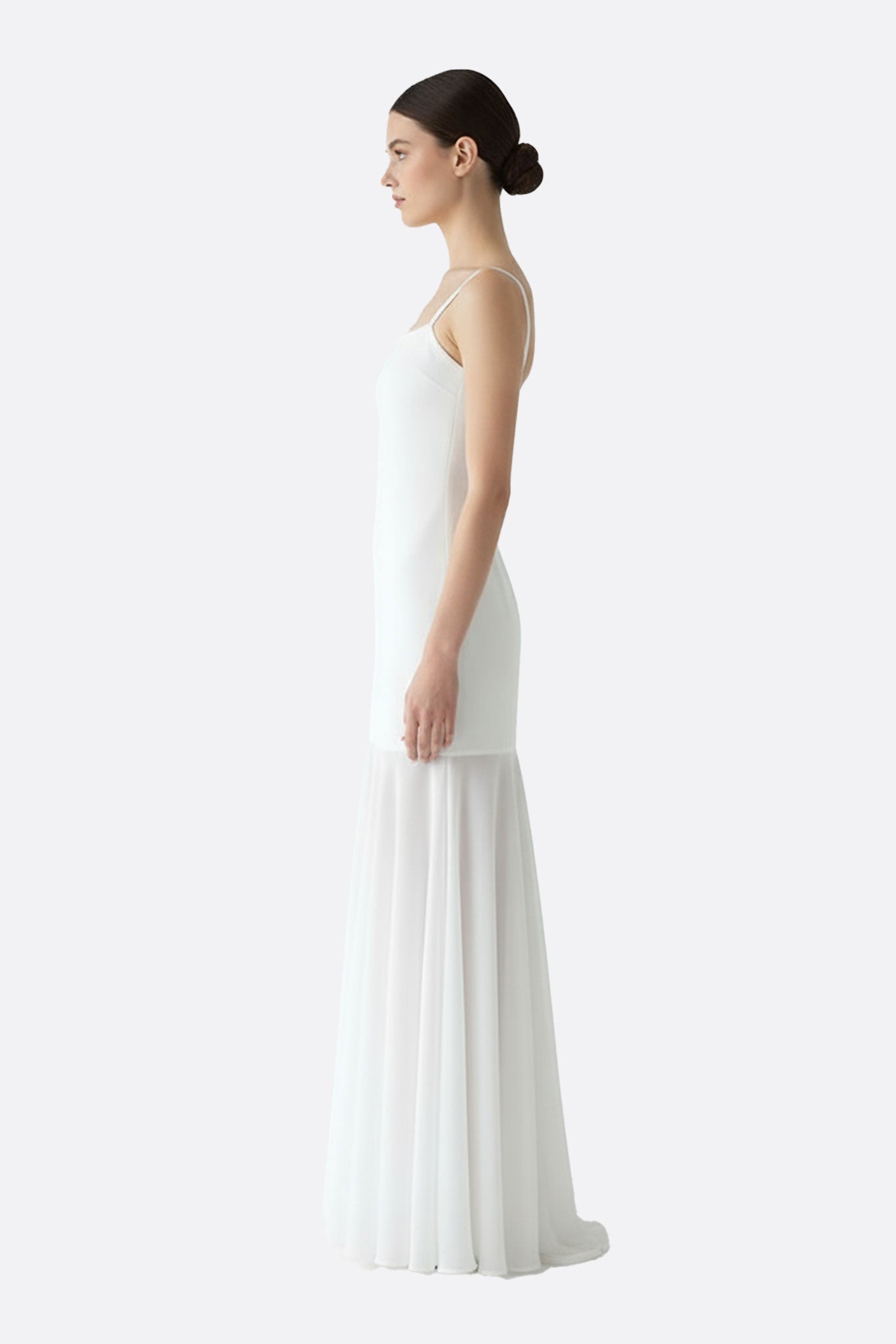 Zoom sur la robe longue blanche à bretelles fines, soulignant la légèreté de sa jupe transparente pour une allure élégante.