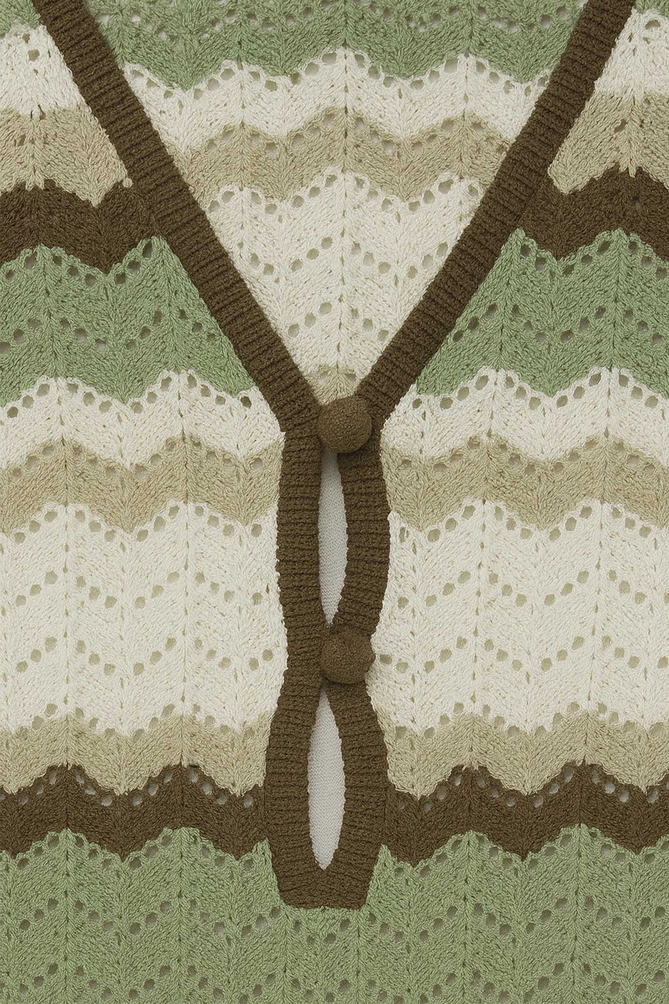 
Détail captivant de la robe longue en crochet vert sauge et ivoire, révélant ses rayures ondulées raffinées et aériennes.



