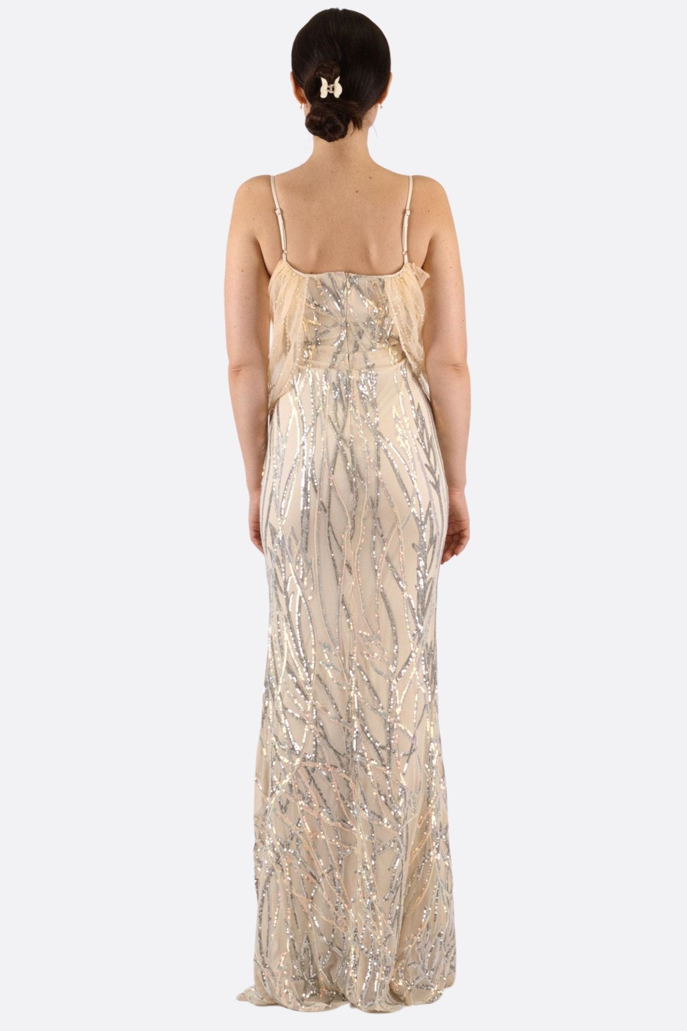 
Robe nude à sequins argentés, vue 3/4 mettant en avant son drapé aérien et sa coupe sirène sophistiquée.



