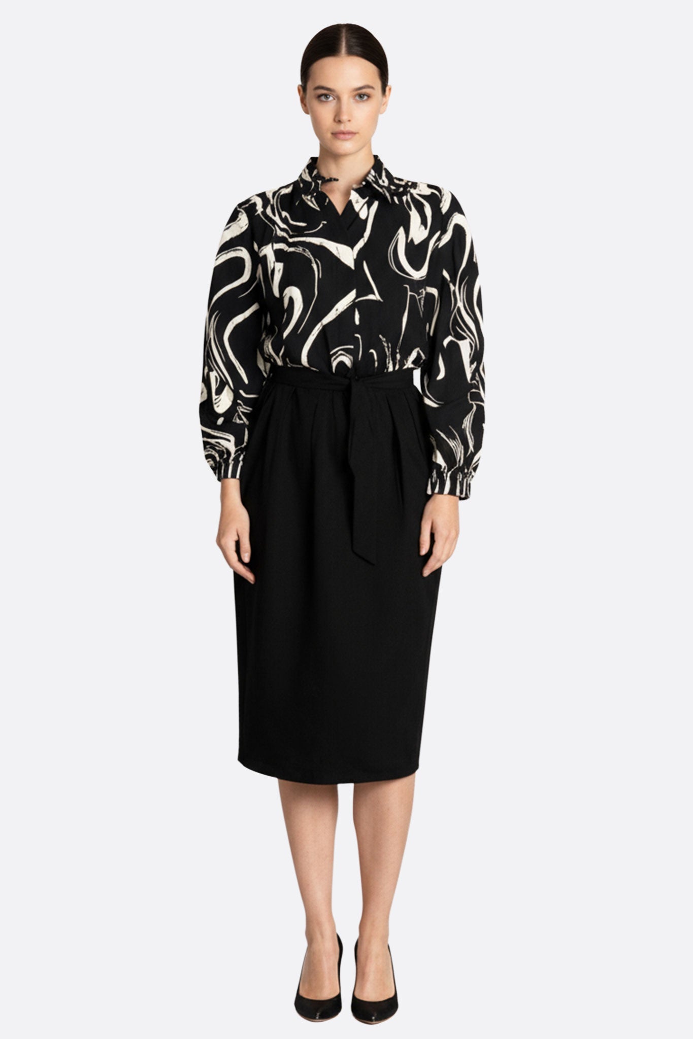 Robe noire mi-longue avec haut à motifs abstraits, ceinture nouée, pour un look chic et artistique.