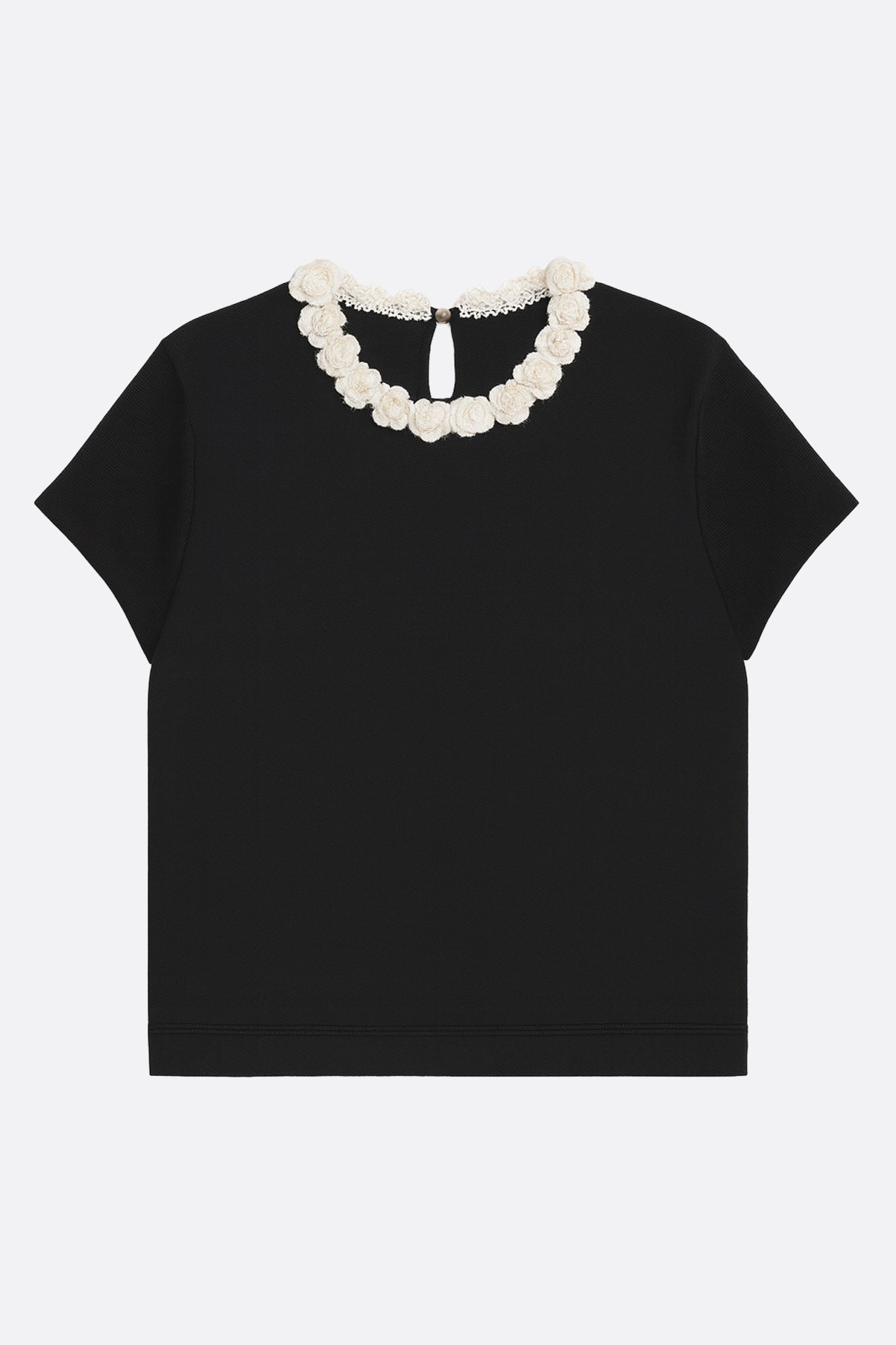 T-shirt negro con cuello de camélias perlados, vista 3/4 mostrando su corte moderno, ideal para un estilo casual y elegante.