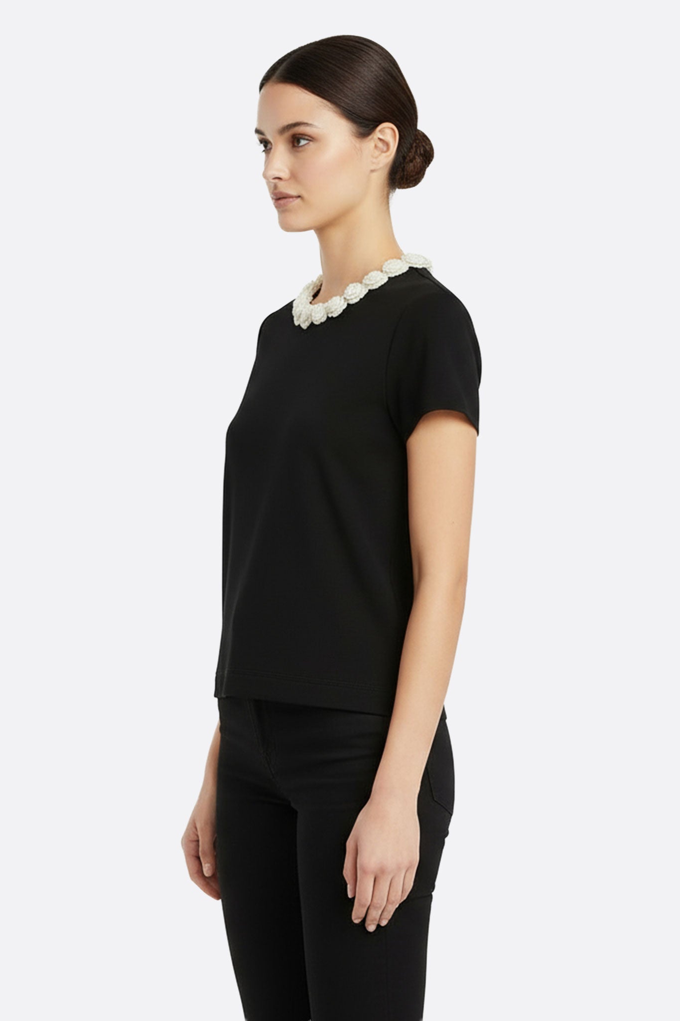 Detalle del cuello de camélias perlados en t-shirt negro, ideal para looks elegantes y ocasiones especiales.