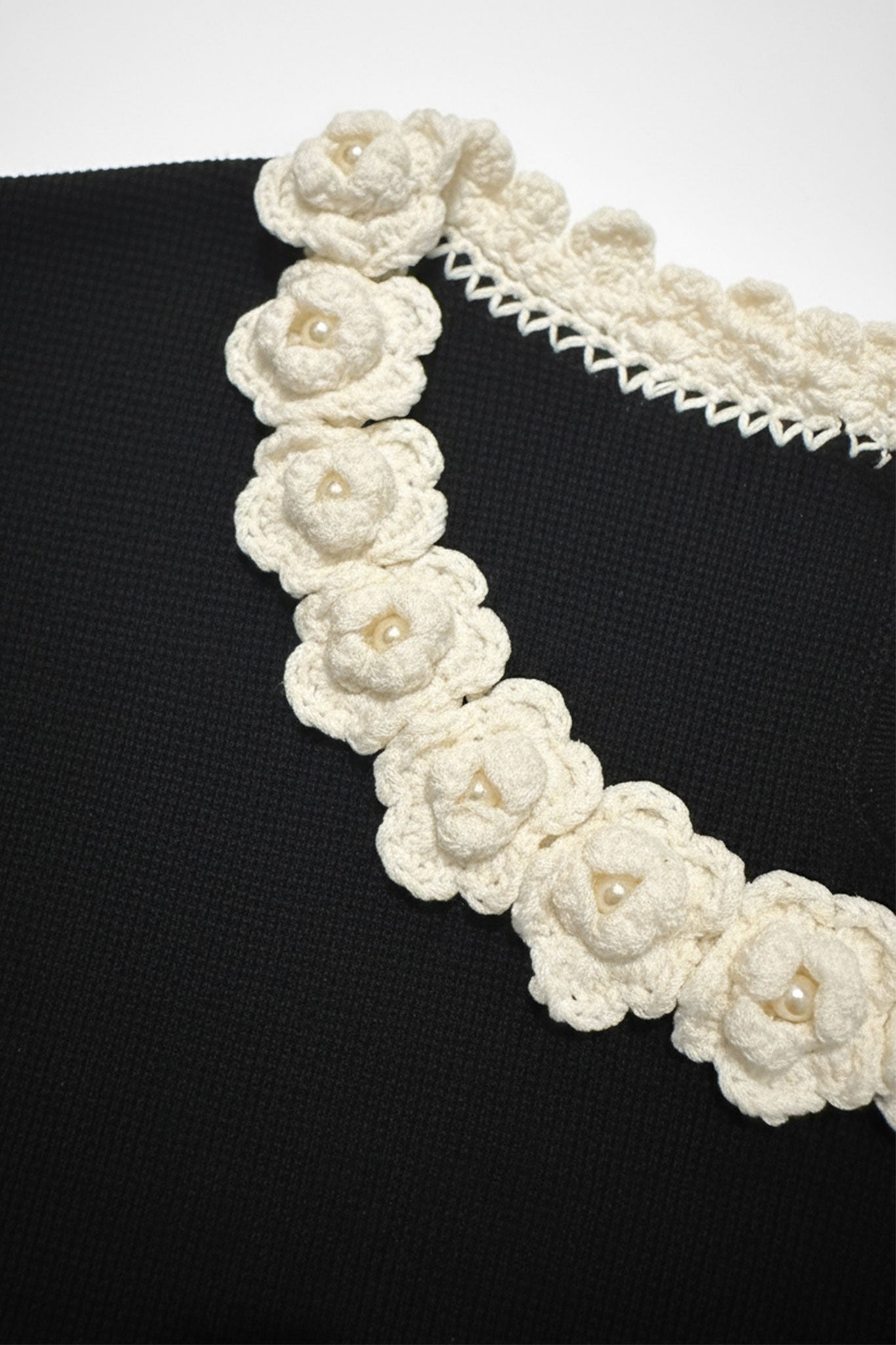 Detalle del cuello de camélias perlados en t-shirt negro, añadiendo un toque de elegancia y sofisticación a tu atuendo.