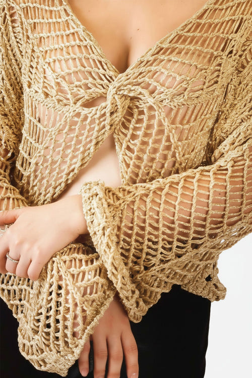 
Détail du haut en maille crochet ajourée beige, mettant en avant sa texture aérée et son élégance pour un style estival.



