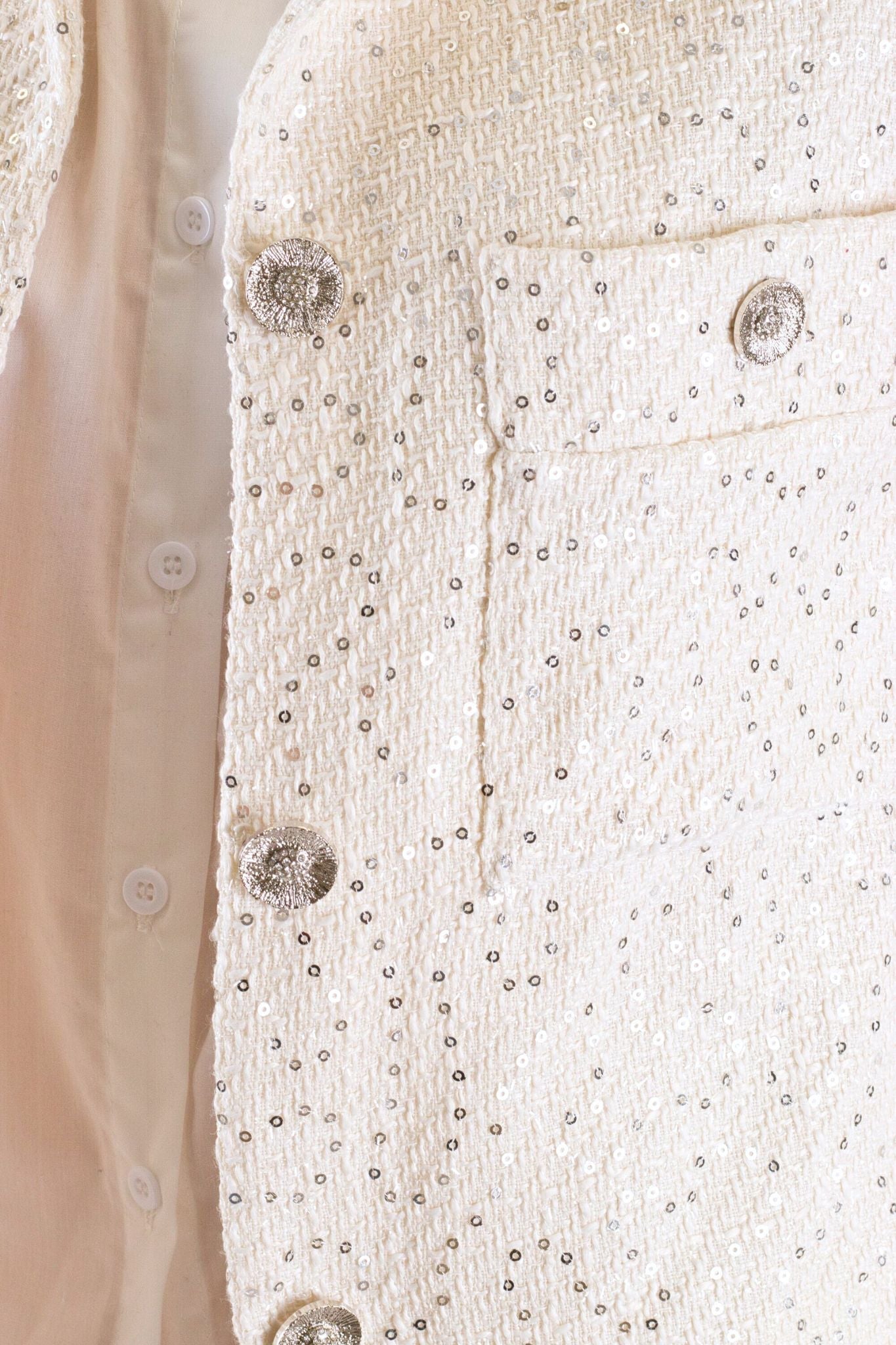Détail d'une veste en tweed blanc agrémentée de sequins, idéale pour une allure chic lors d'événements élégants.