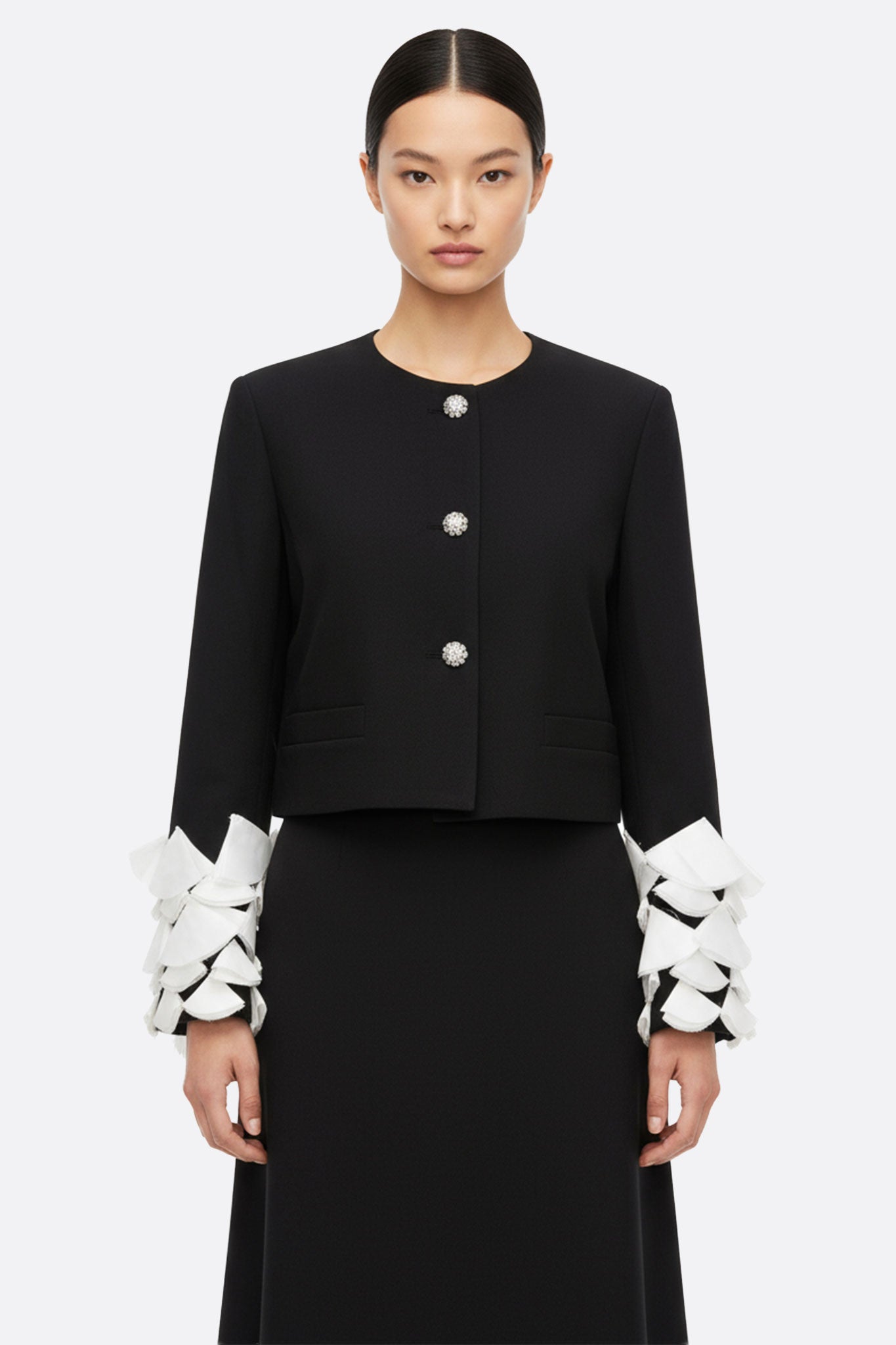 Veste noire élégante aux manches pétales rehaussées de plumes blanches, idéale pour sublimer une tenue de soirée.