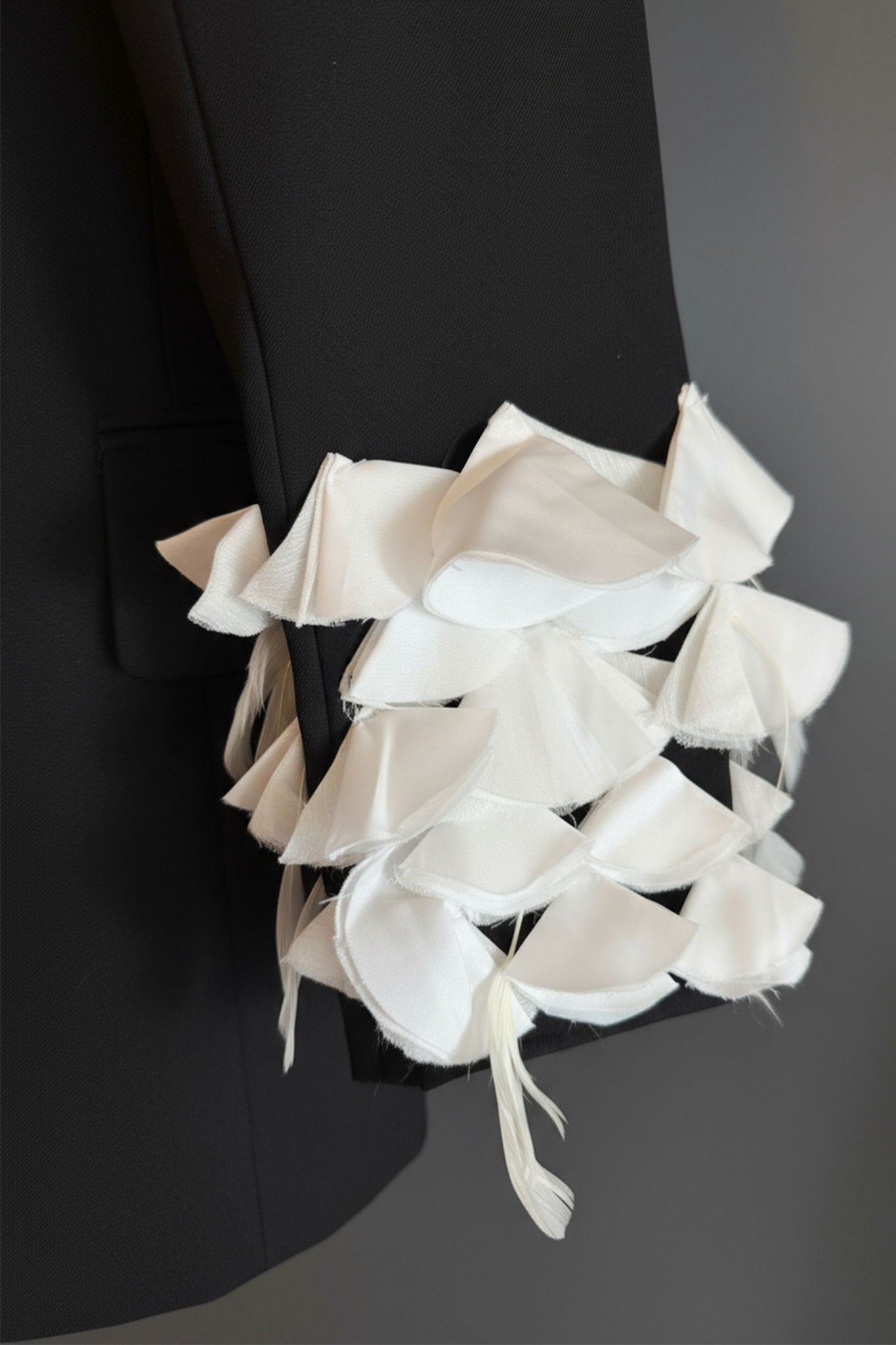 
Détail de la veste noire avec manches en pétales et plumes blanches, un choix raffiné pour une soirée élégante.




