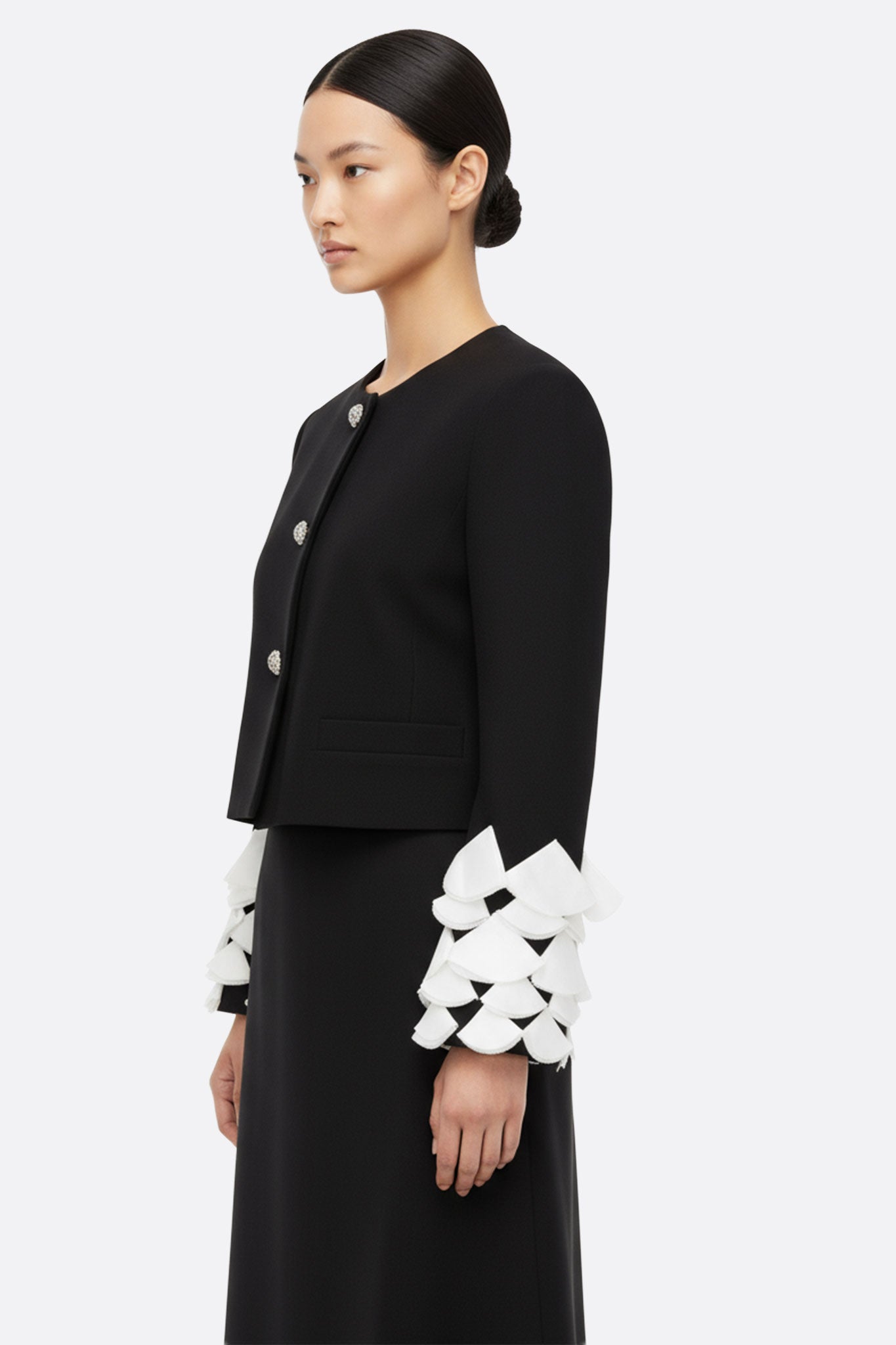 Zoom sur les manches en pétales de la veste noire, embellies de plumes blanches, un détail enchanteur pour un look raffiné.