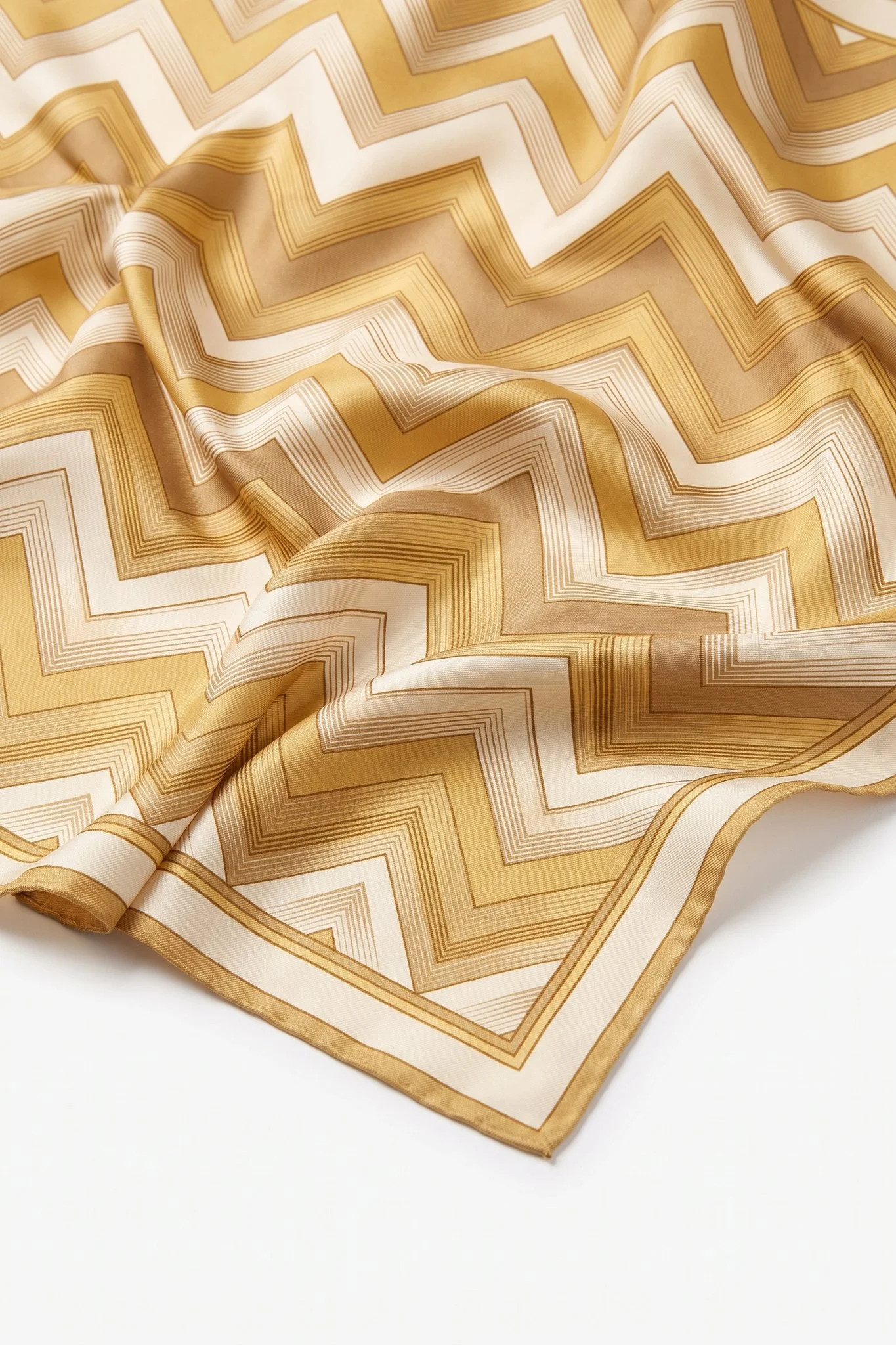 Gros plan sur les plis du carré de soie Chevrons d'or, twill de soie et bord roulotté main