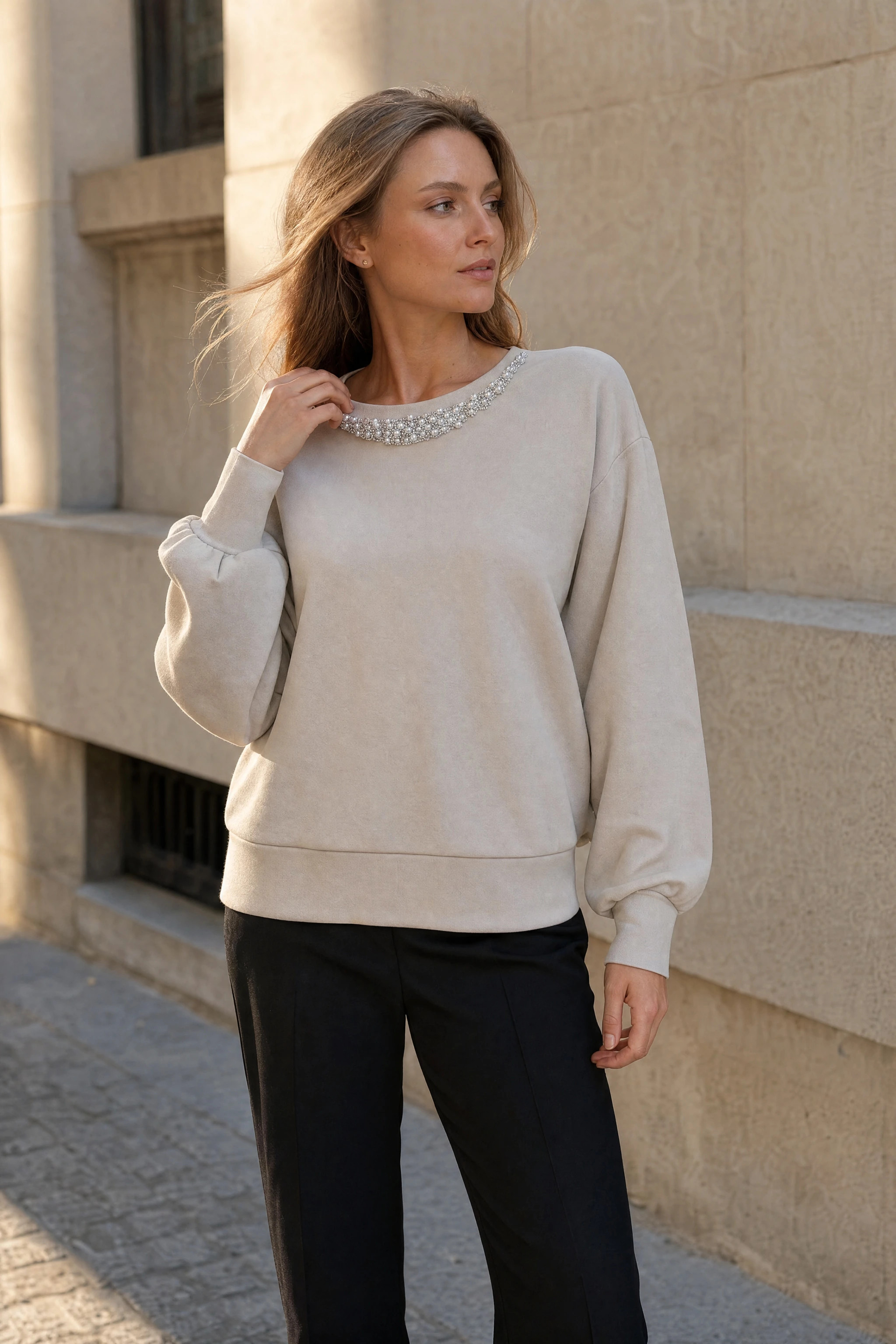 Pull beige oversize à encolure perlée porté en extérieur dans une rue de vieille ville à la lumière du soir
