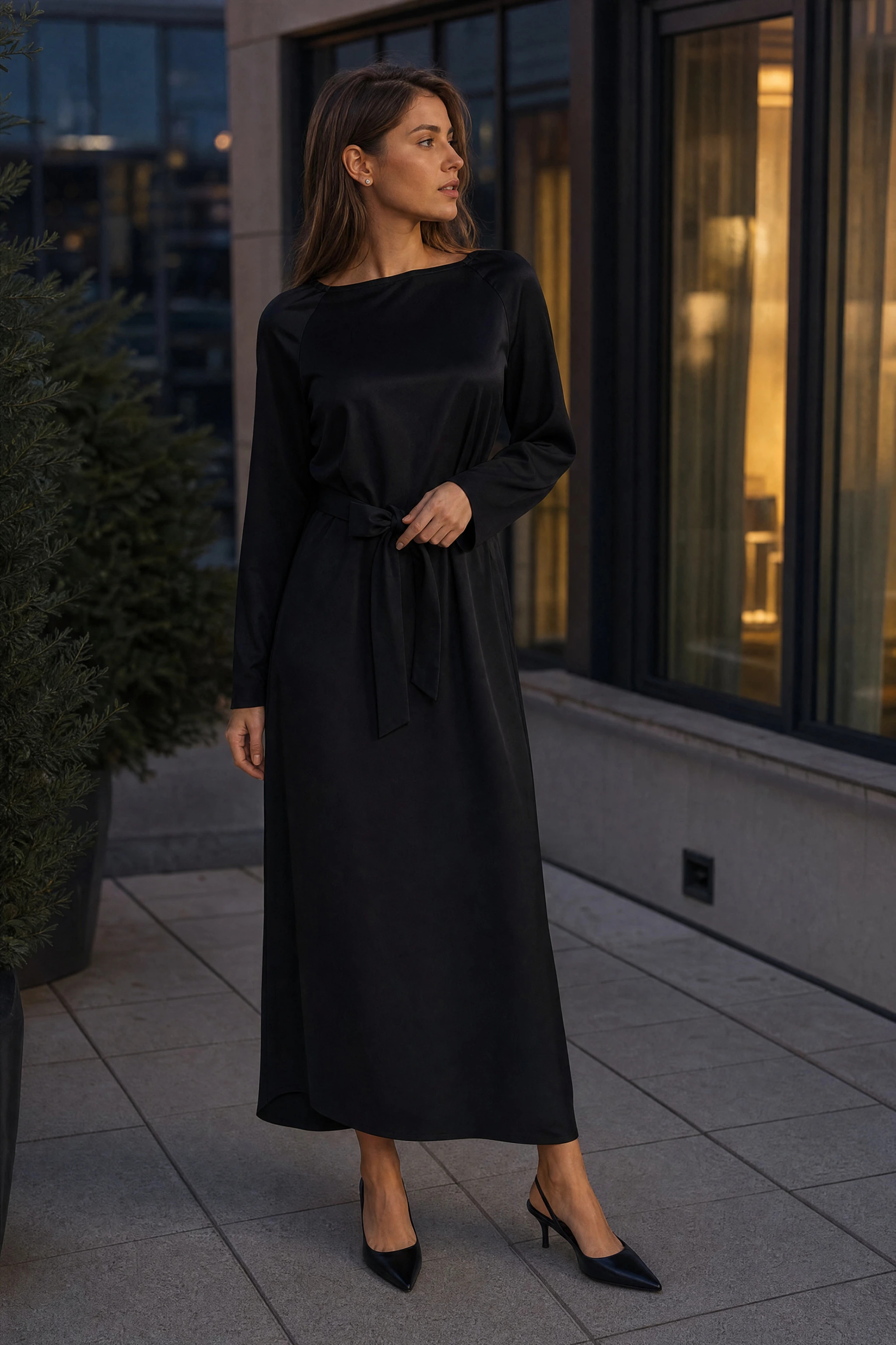 Langes schwarzes Kleid in Satinoptik, im Freien auf einer Stadtterrasse zur blauen Stunde getragen